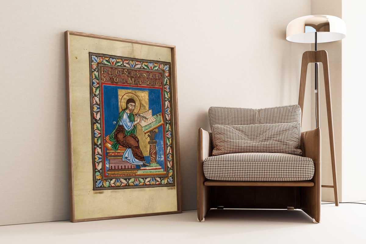 Framed art print of Gospel Book: Saint Matthew, leaning against a wall beside an armchair and a floor lamp