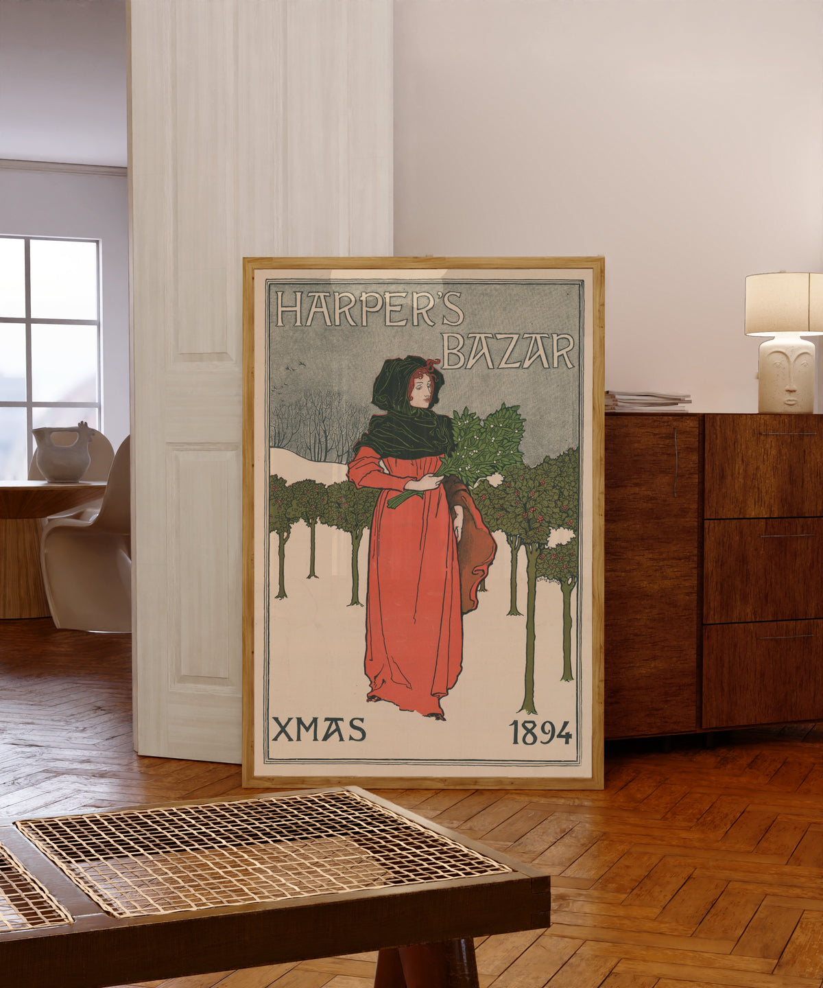 Framed art print of Harper's Bazar, Xmas 1894 by Louis Rhead, in a light wood frame leaning in a warm room with a parquet floor
