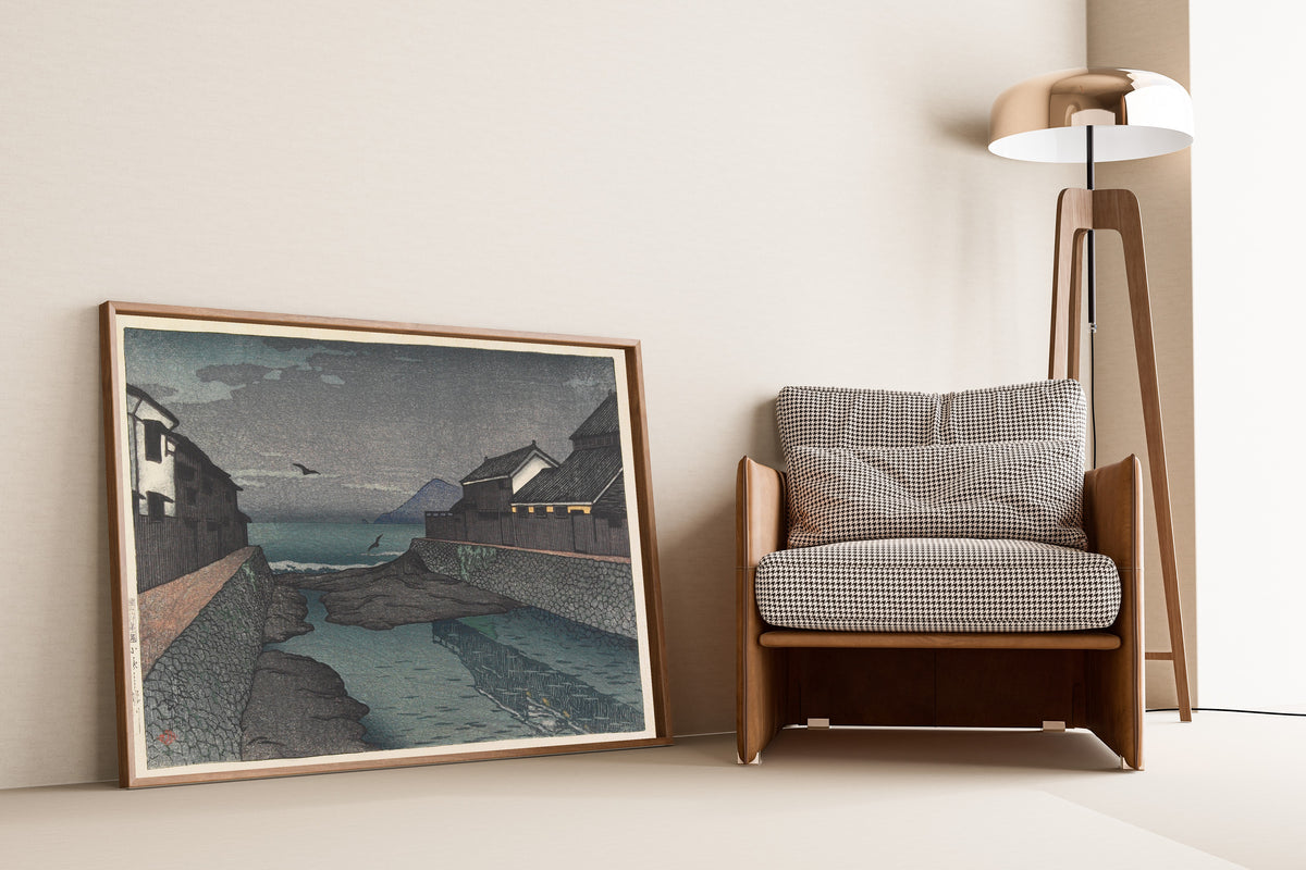Framed art print of Hori River, Obama by Kawase Hasui, leaning against a wall beside an armchair and a floor lamp