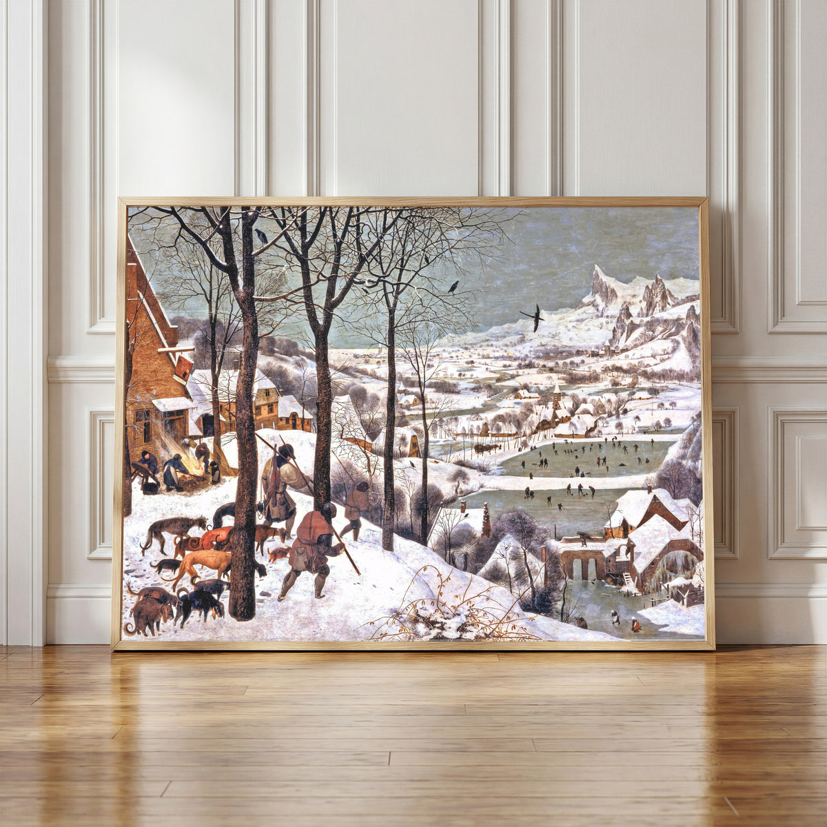 Framed art print of Hunters in the Snow (Winter) by Pieter Bruegel the Elder, in a light wood frame leaning against a panelled white wall