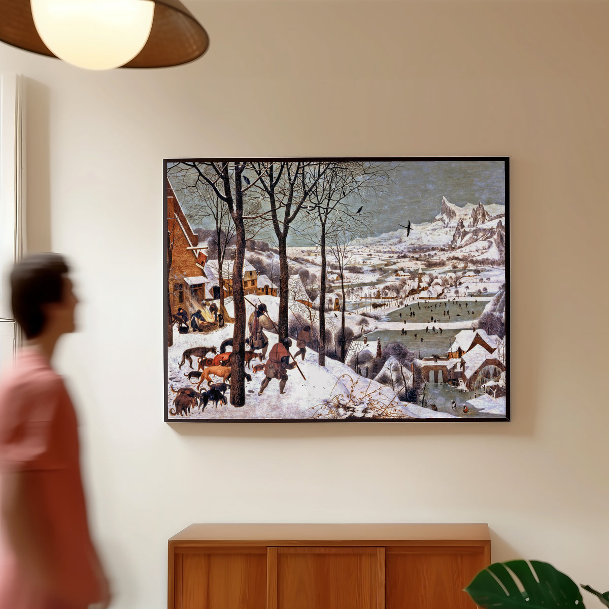Framed art print of Hunters in the Snow (Winter) by Pieter Bruegel the Elder, in a slim black frame on a warm wall in a sunlit room