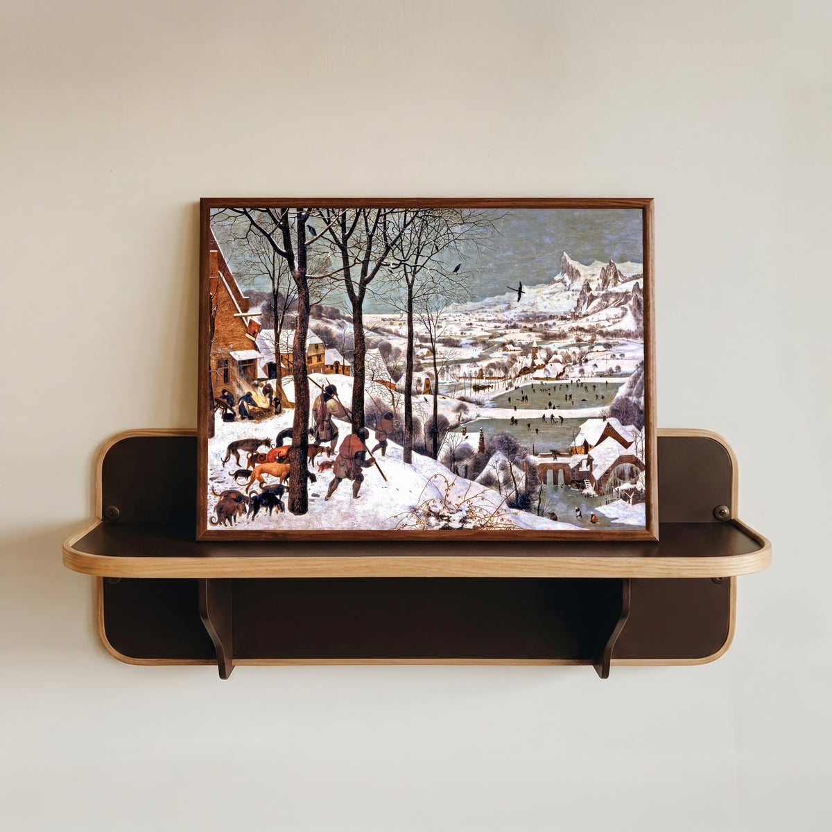 Framed art print of Hunters in the Snow (Winter) by Pieter Bruegel the Elder, in a dark wood frame resting on a wall shelf