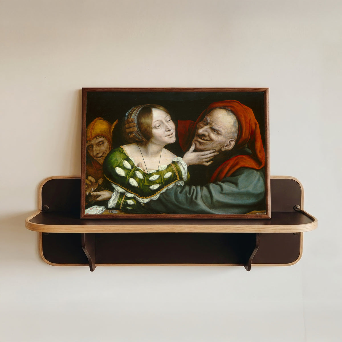 Framed art print of Ill-Matched Lovers by Quinten Massys, in a dark wood frame resting on a wall shelf
