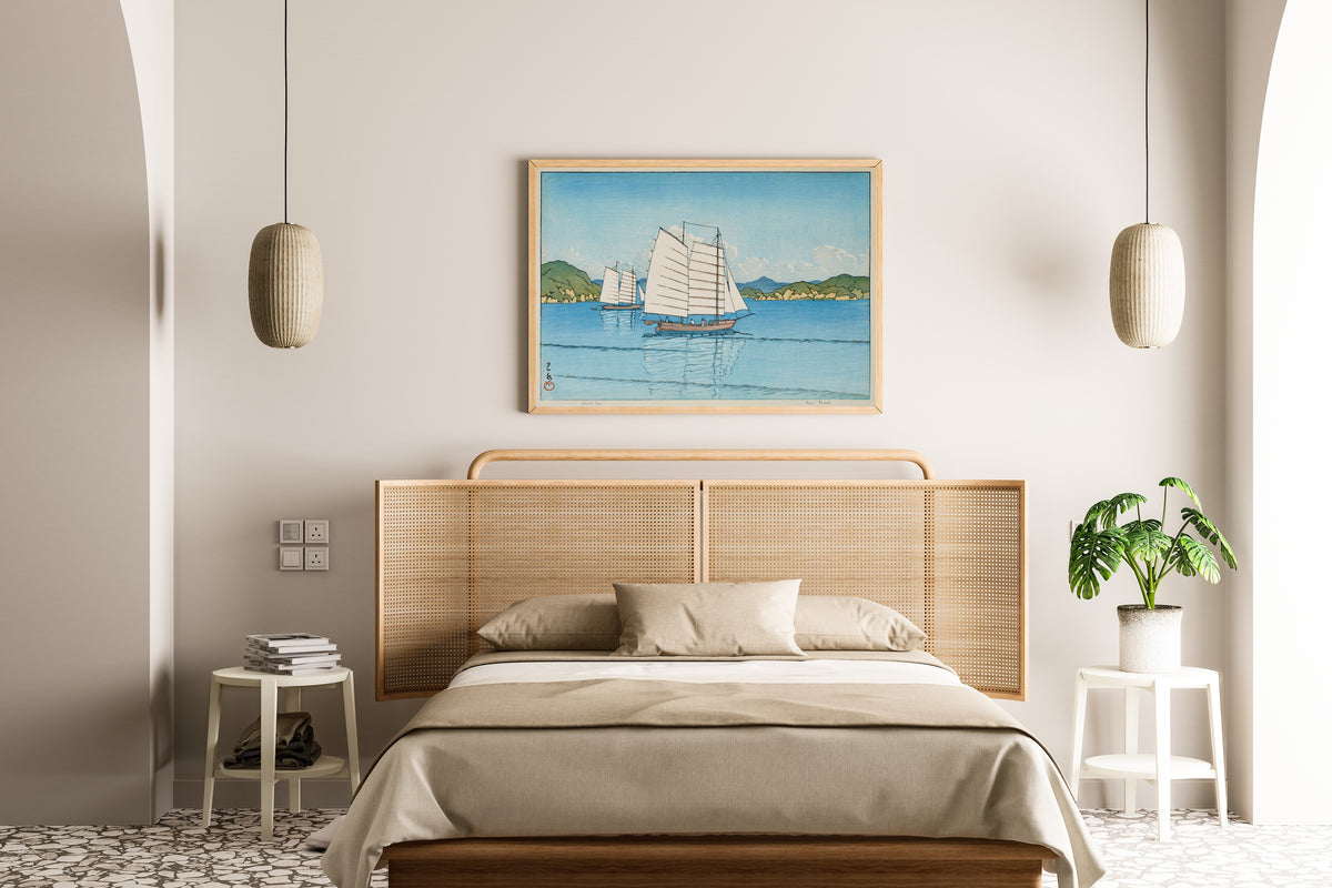 Framed art print of Inland Sea by Kawase Hasui, above a cane-headboard bed