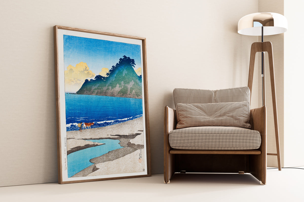 Framed art print of Iwai Beach, Awa Province by Kawase Hasui, leaning against a wall beside an armchair and a floor lamp