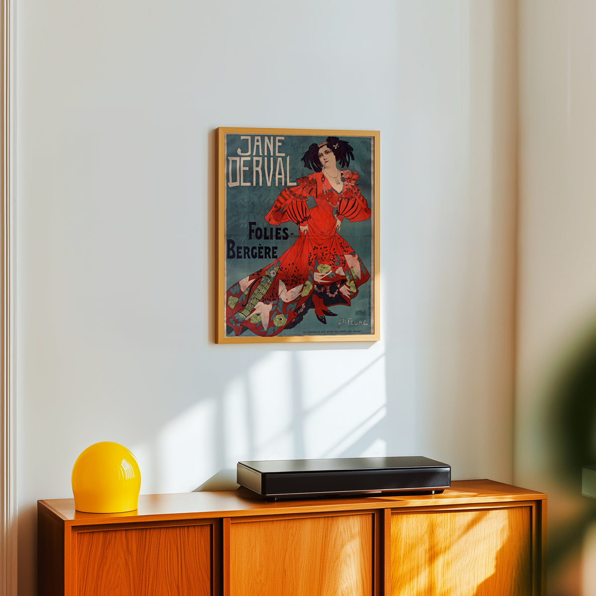 Framed art print of Jane Derval, Folies-Bergère by Georges de Feure, in a light wood frame on a white wall above an orange sideboard