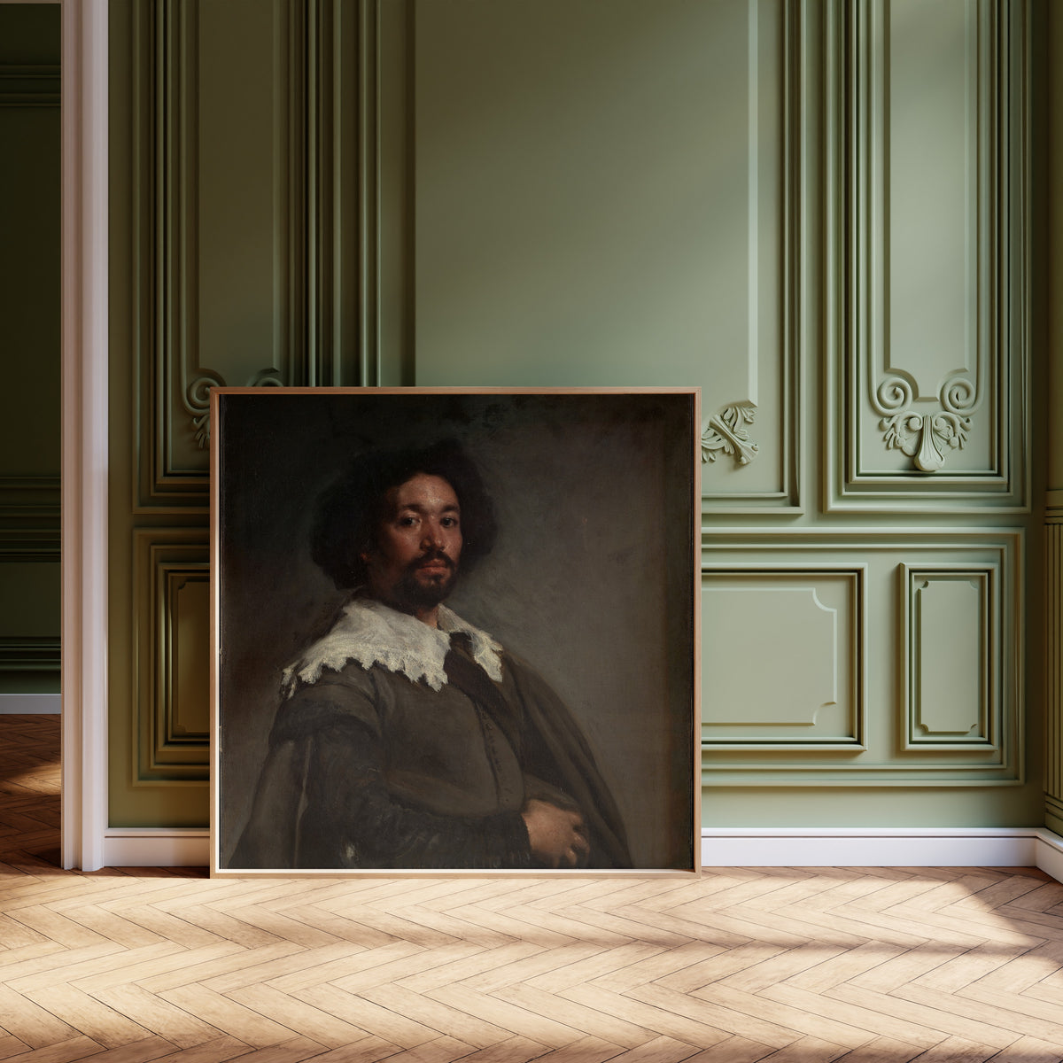 Framed art print of Juan de Pareja by Diego Velázquez, leaning against olive-green panelling on a herringbone floor