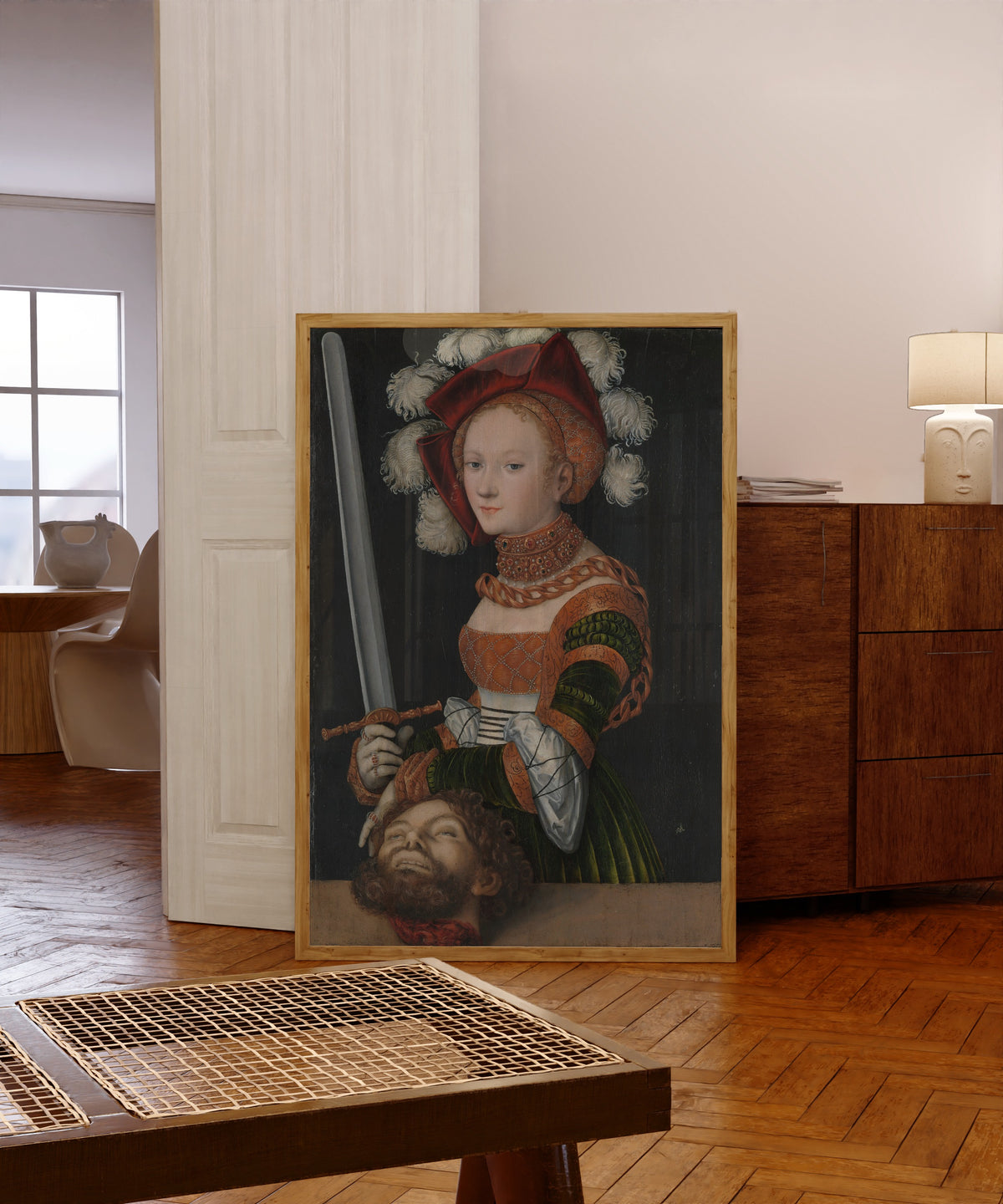 Framed art print of Judith with the Head of Holofernes by Lucas Cranach the Elder, in a light wood frame leaning in a warm room with a parquet floor