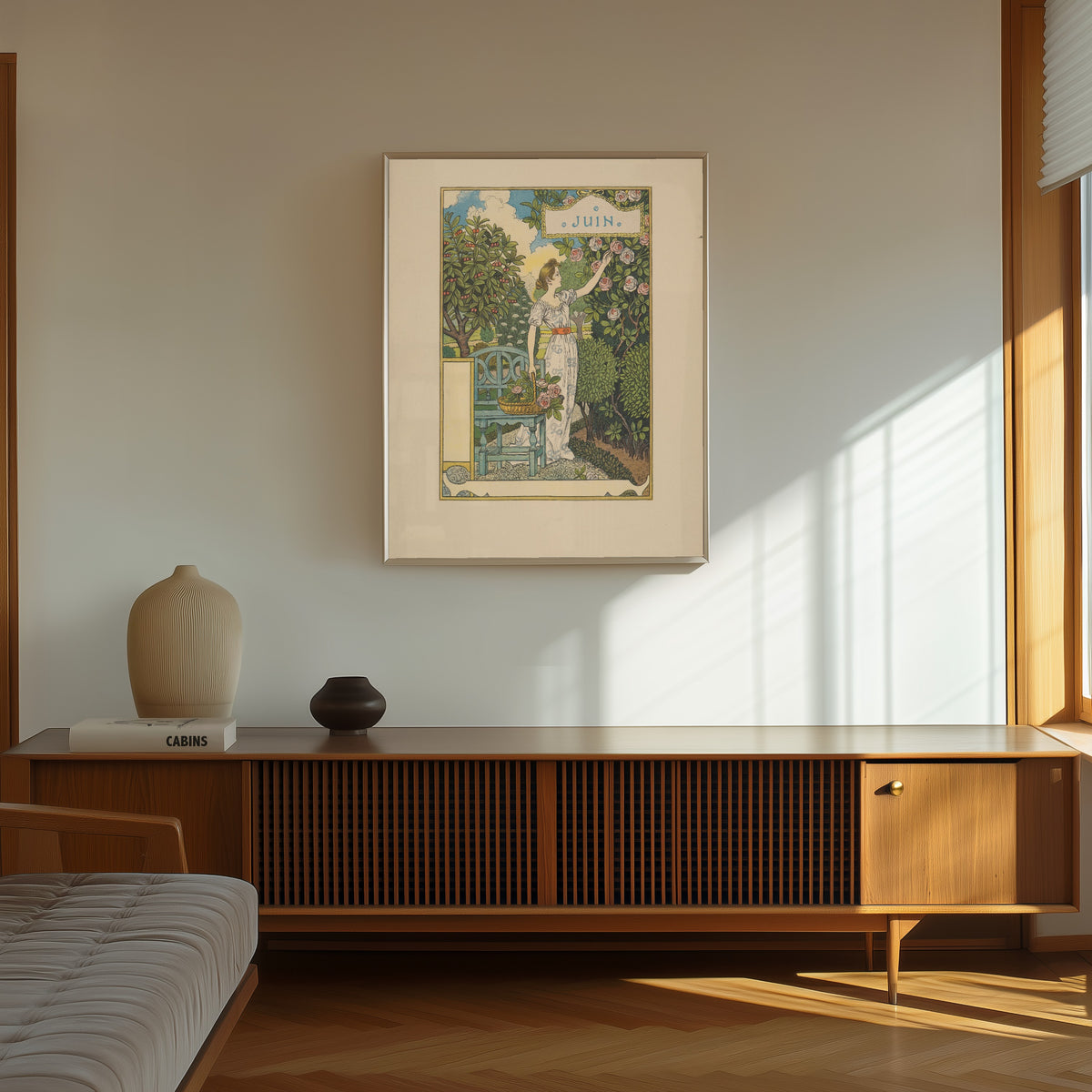 Framed art print of Juin by Eugène Grasset, in a thin light frame on a sunlit wall above a wooden sideboard