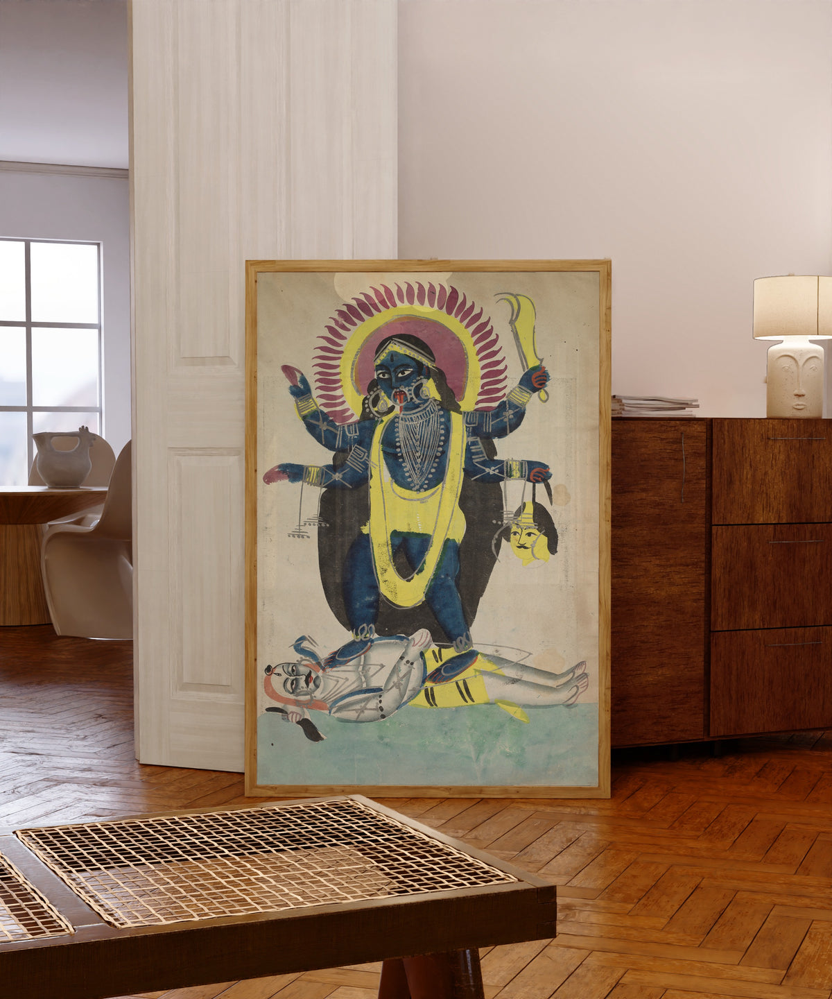 Framed art print of Kali Dancing on Shiva by Kalighat painter, in a light wood frame leaning in a warm room with a parquet floor