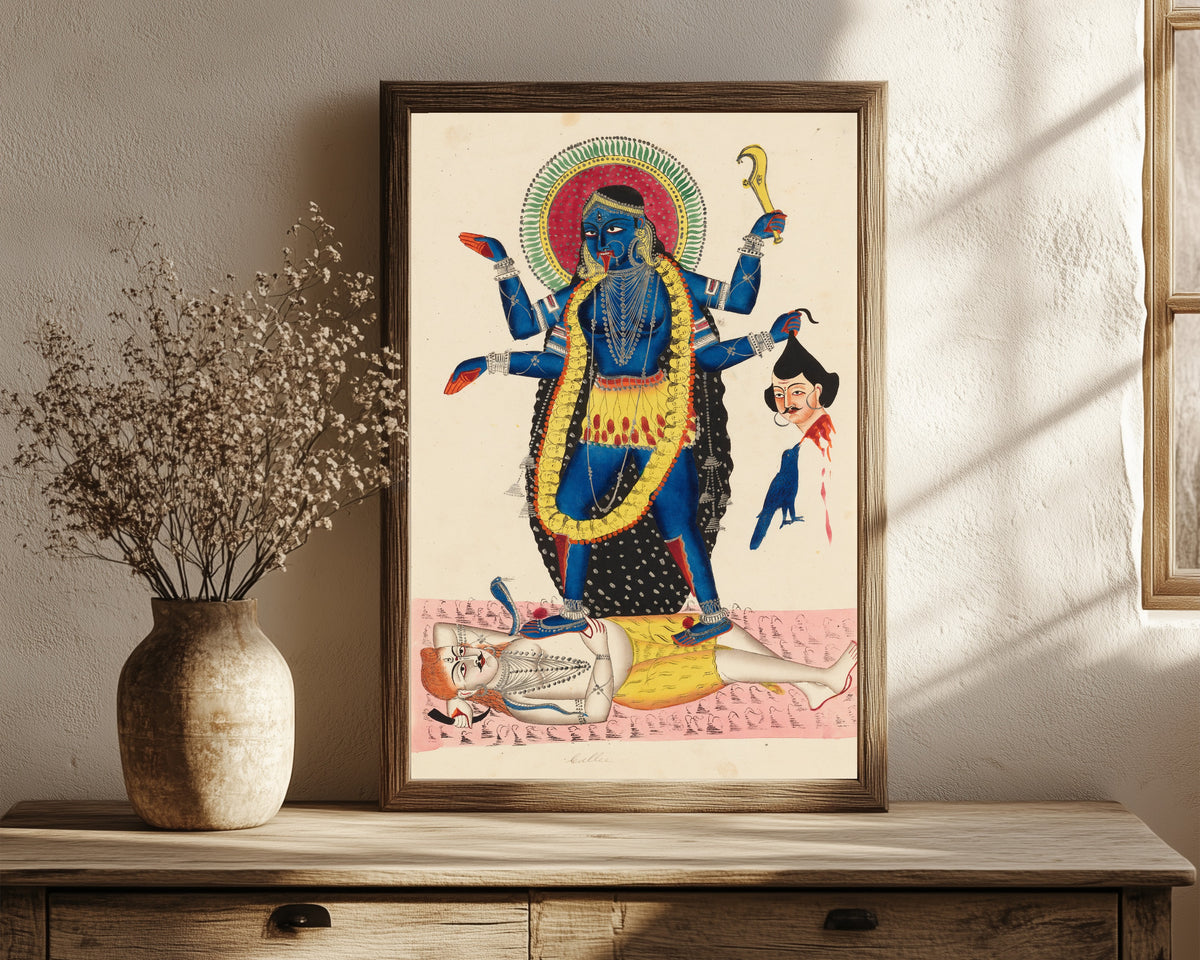 Framed art print of Kali Trampling Upon Shiva by Kalighat painter, in a dark wood frame leaning on a rustic console beside dried flowers