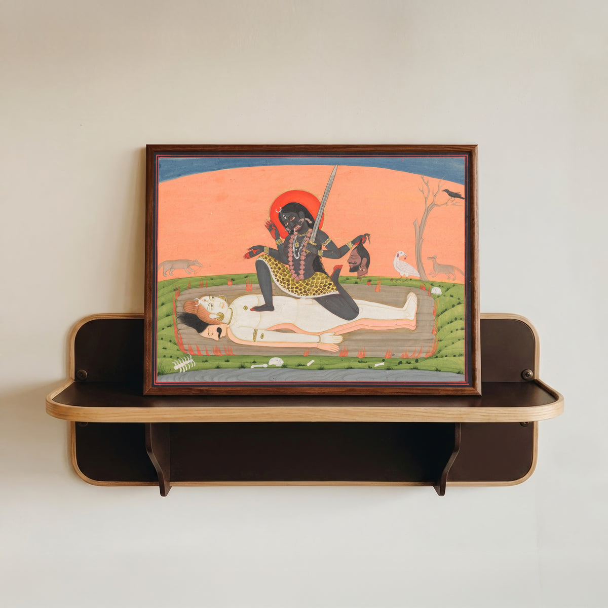 Framed art print of Kali on Shiva by Pahari school, in a dark wood frame resting on a wall shelf