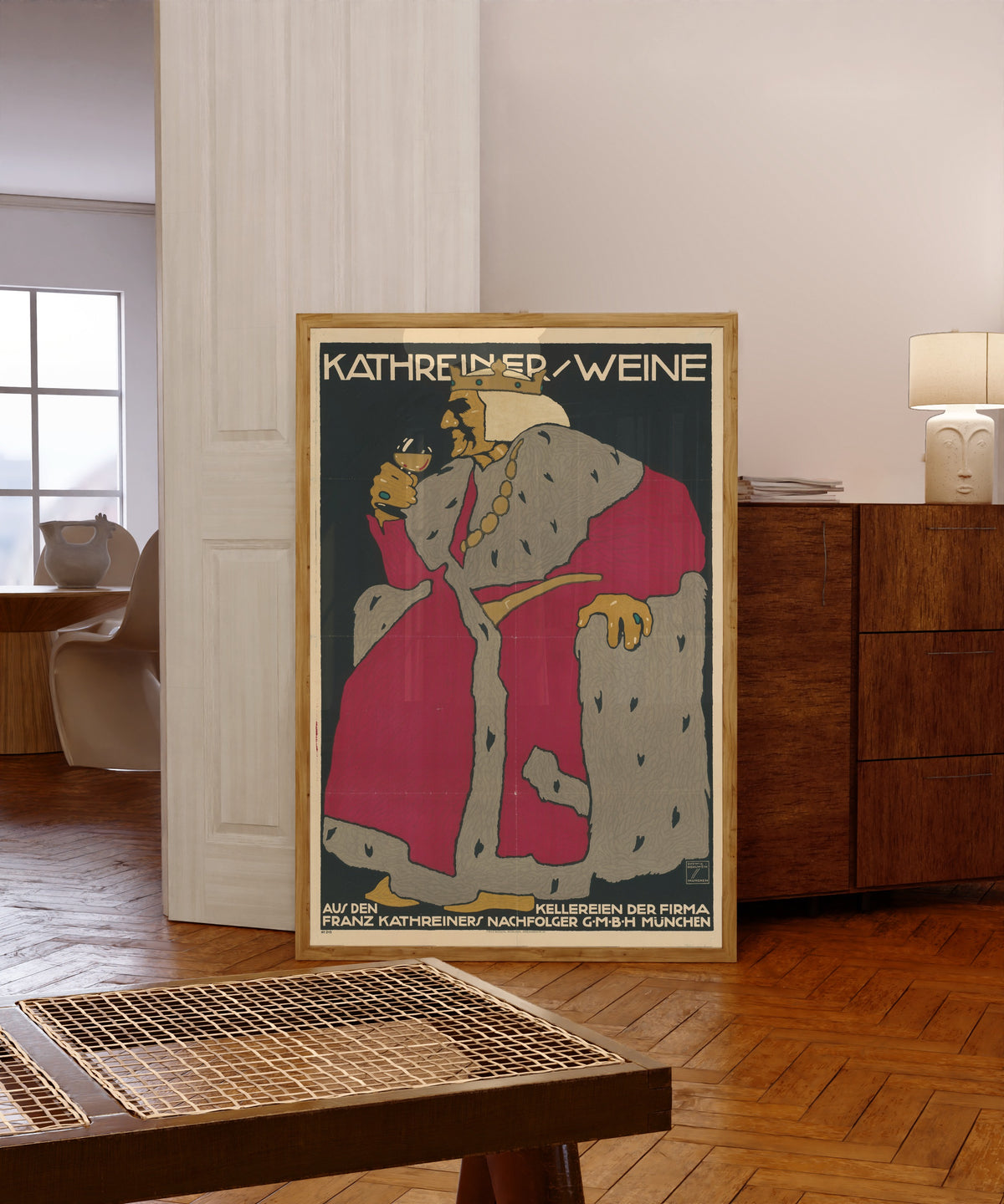 Framed art print of Kathreiner Weine by Ludwig Hohlwein, in a light wood frame leaning in a warm room with a parquet floor