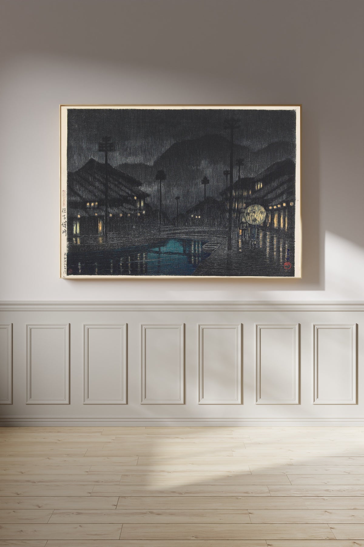 Framed art print of Kinosaki in Tajima Province by Kawase Hasui, on a panelled wall in afternoon light