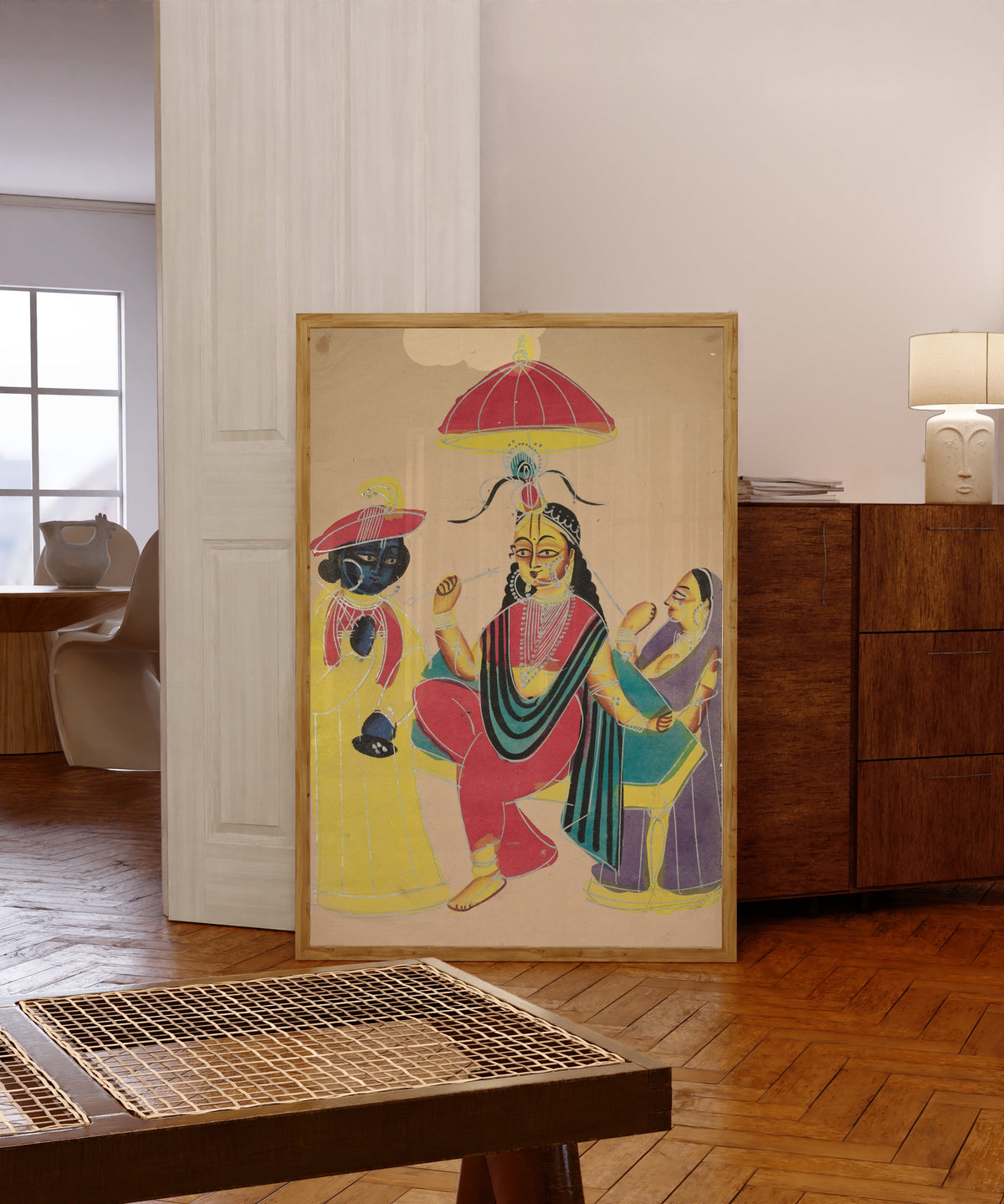 Framed art print of Krishna Standing by Radha who is Seated on a Chair by Kalighat painter, in a light wood frame leaning in a warm room with a parquet floor
