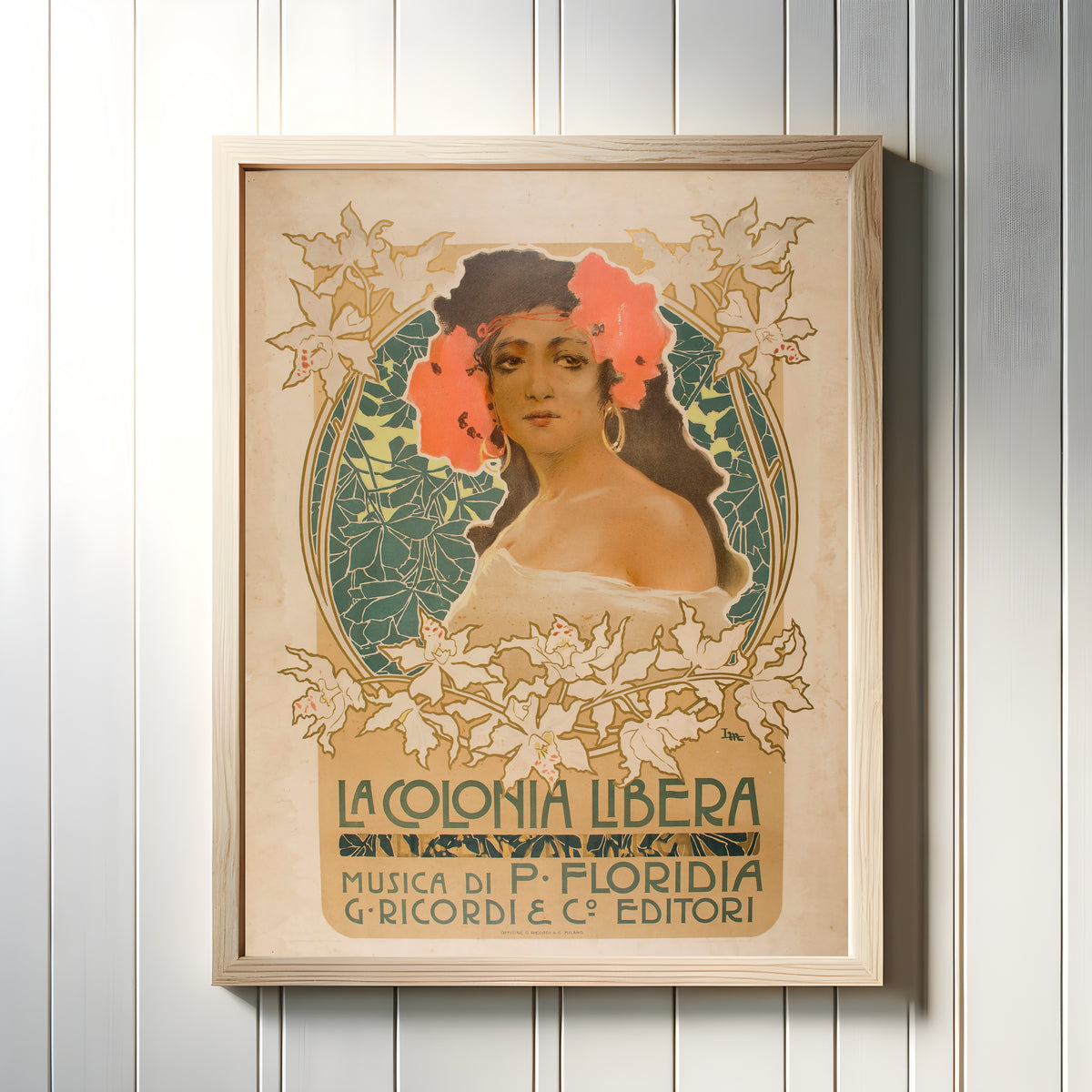 Framed art print of La Colonia Libera by Leopoldo Metlicovitz, in a light wood frame on a white panelled wall