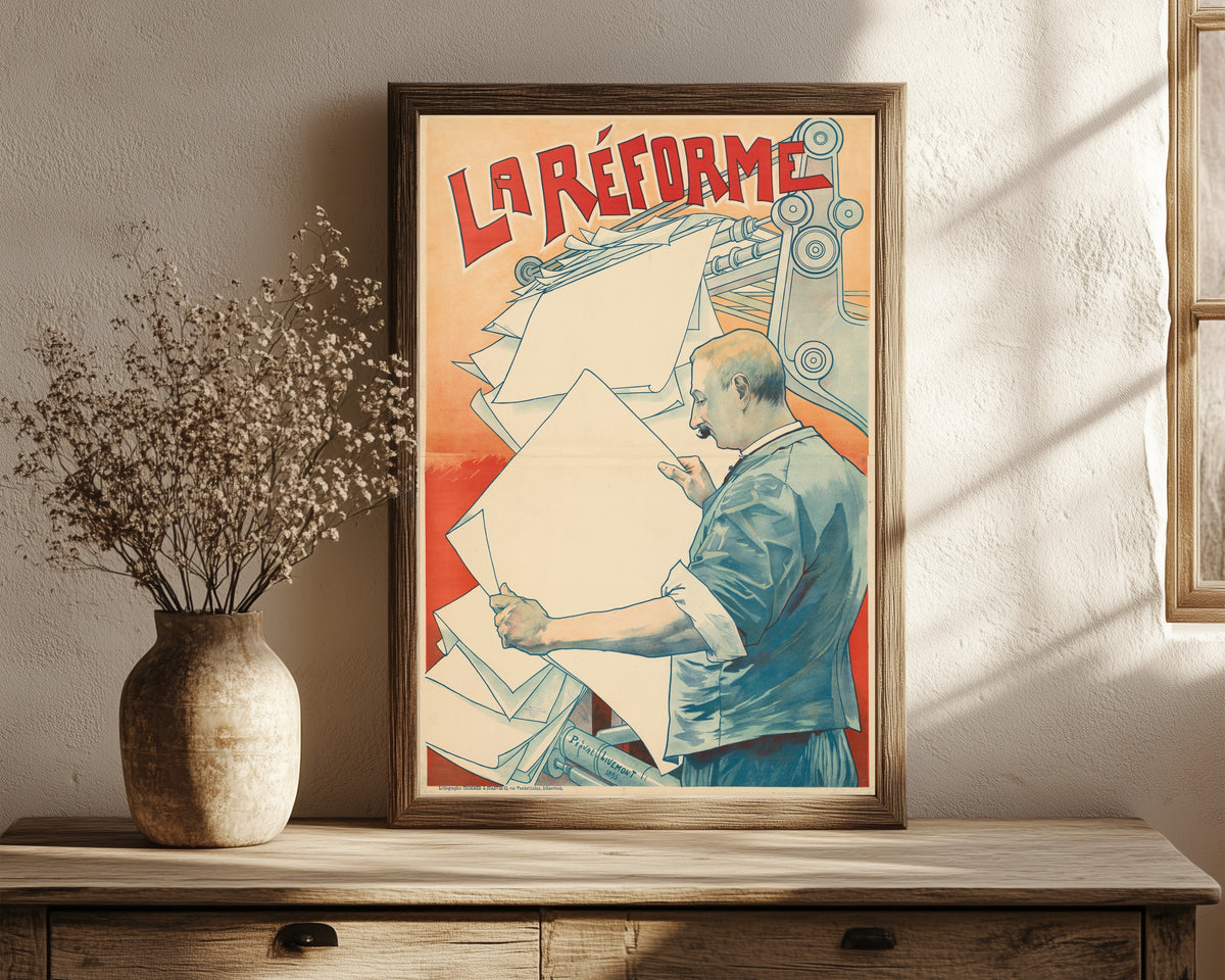 Framed art print of La Réforme by Henri Privat-Livemont, in a dark wood frame leaning on a rustic console beside dried flowers