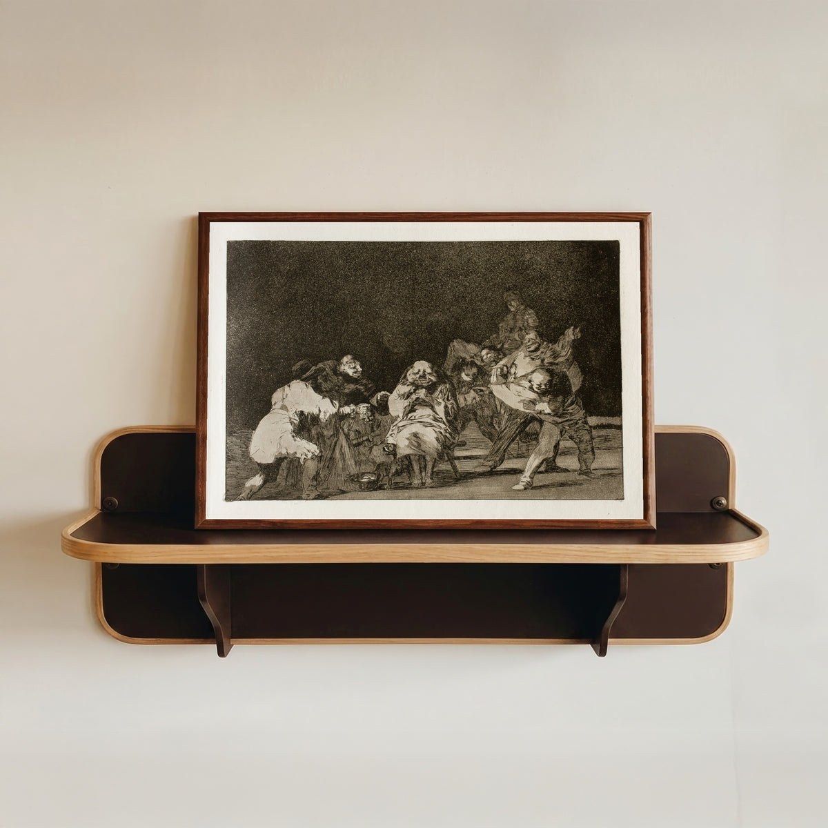 Framed art print of La lealtad (Loyalty), from Los Disparates by Francisco de Goya, in a dark wood frame resting on a wall shelf