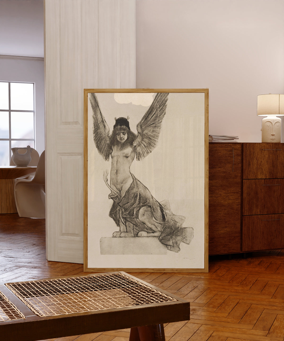 Framed art print of La sphynge ou Parallèlement by Félicien Rops, in a light wood frame leaning in a warm room with a parquet floor