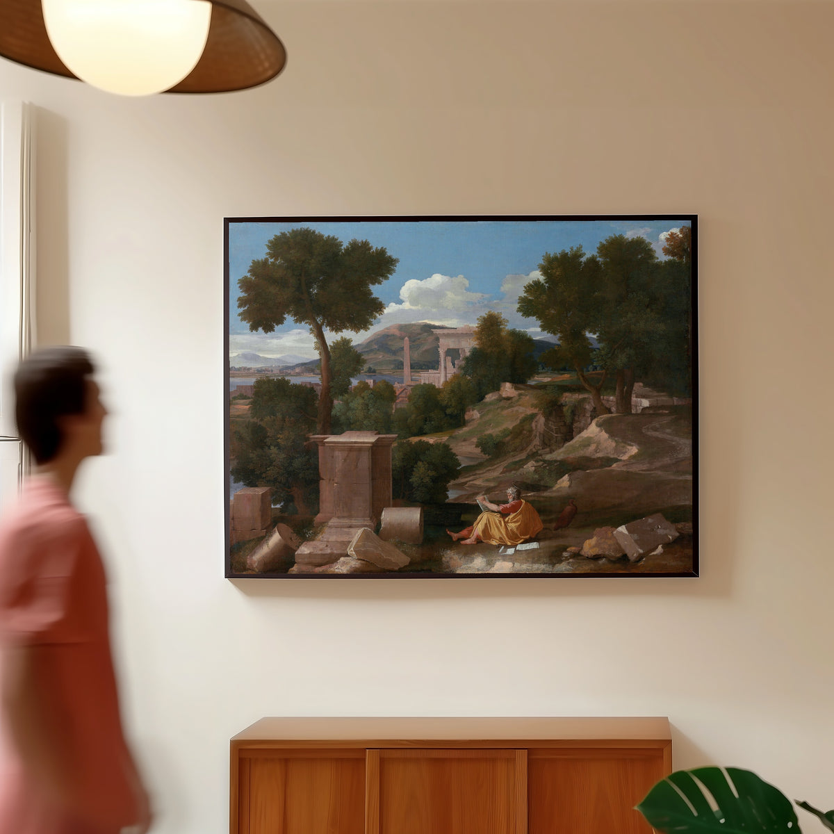 Framed art print of Landscape with Saint John on Patmos by Nicolas Poussin, in a slim black frame on a warm wall in a sunlit room