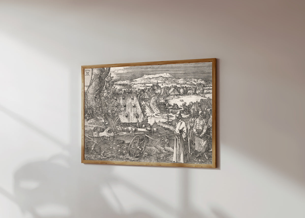 Framed art print of Landscape with the Cannon by Albrecht Dürer, in a light wood frame on a sunlit white wall, seen at a slight angle