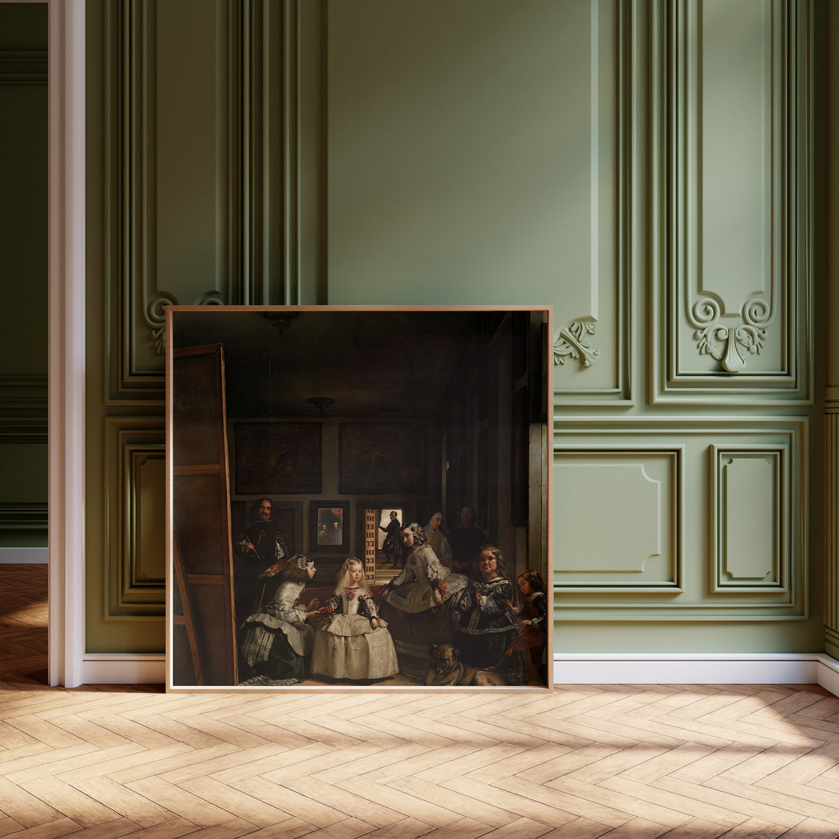 Framed art print of Las Meninas by Diego Velázquez, leaning against olive-green panelling on a herringbone floor