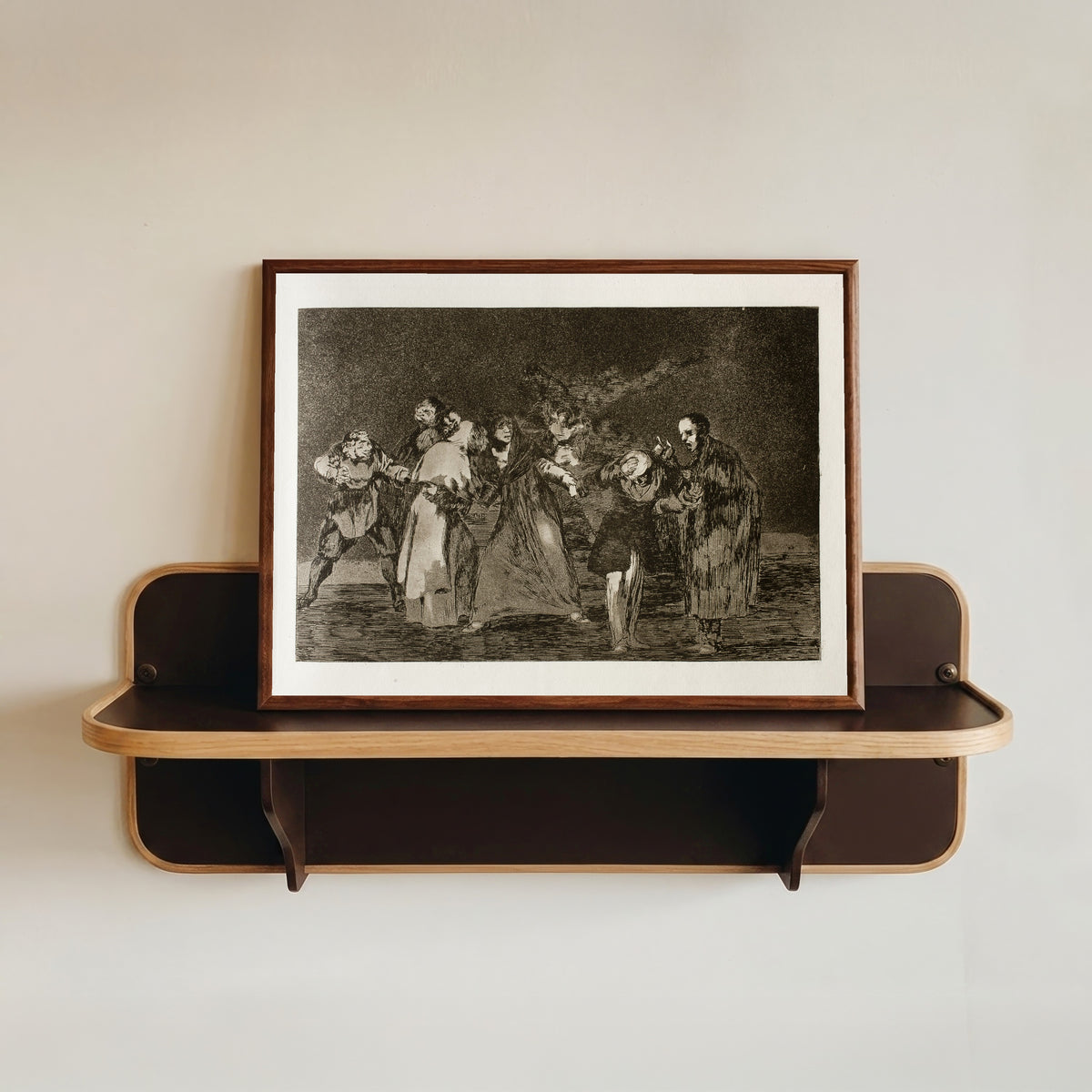 Framed art print of Las exhortaciones (The Exhortations), from Los Disparates by Francisco de Goya, in a dark wood frame resting on a wall shelf
