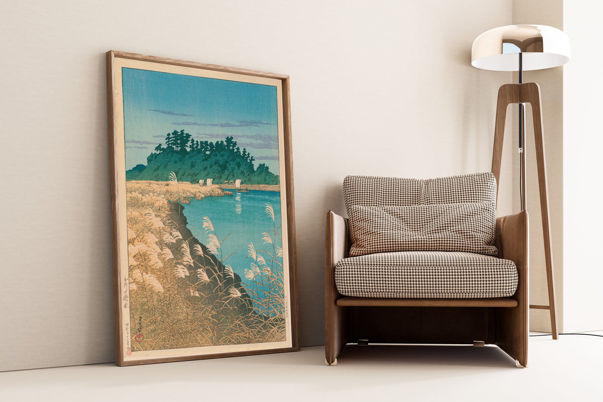 Framed art print of Late Autumn in Ichikawa by Kawase Hasui, leaning against a wall beside an armchair and a floor lamp