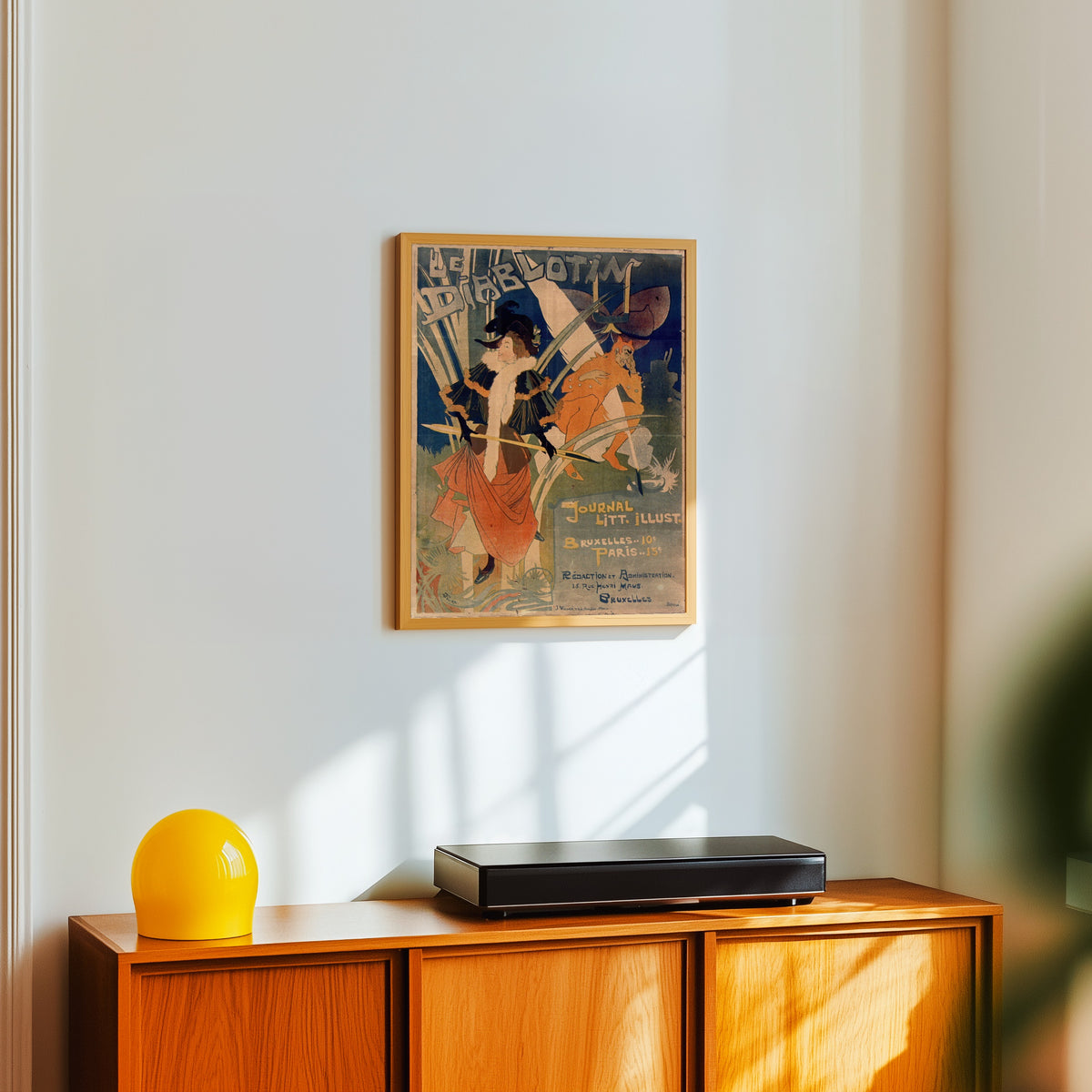 Framed art print of Le Diablotin by Georges de Feure, in a light wood frame on a white wall above an orange sideboard