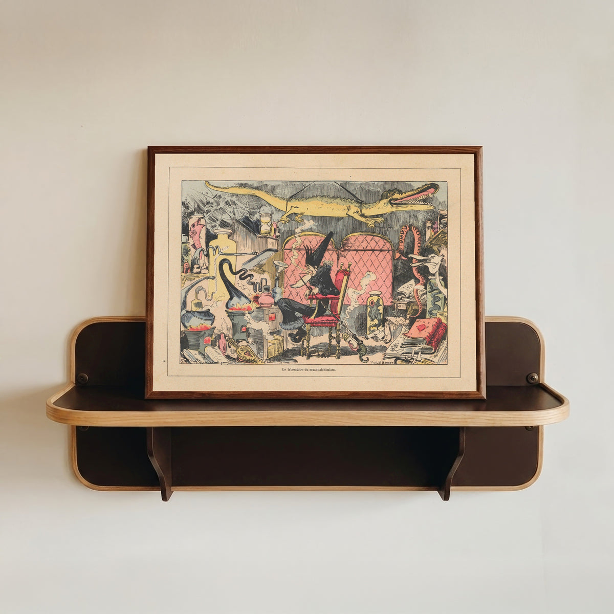 Framed art print of Le laboratoire du savant alchimiste by Albert Robida, in a dark wood frame resting on a wall shelf