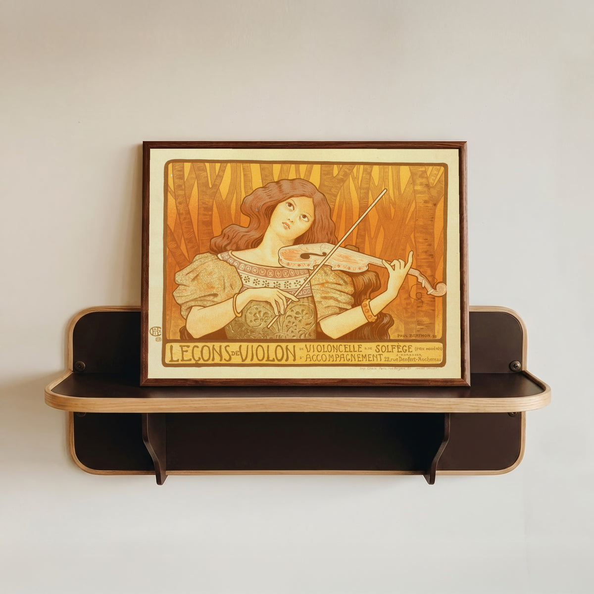 Framed art print of Leçons de Violon by Paul Berthon, in a dark wood frame resting on a wall shelf