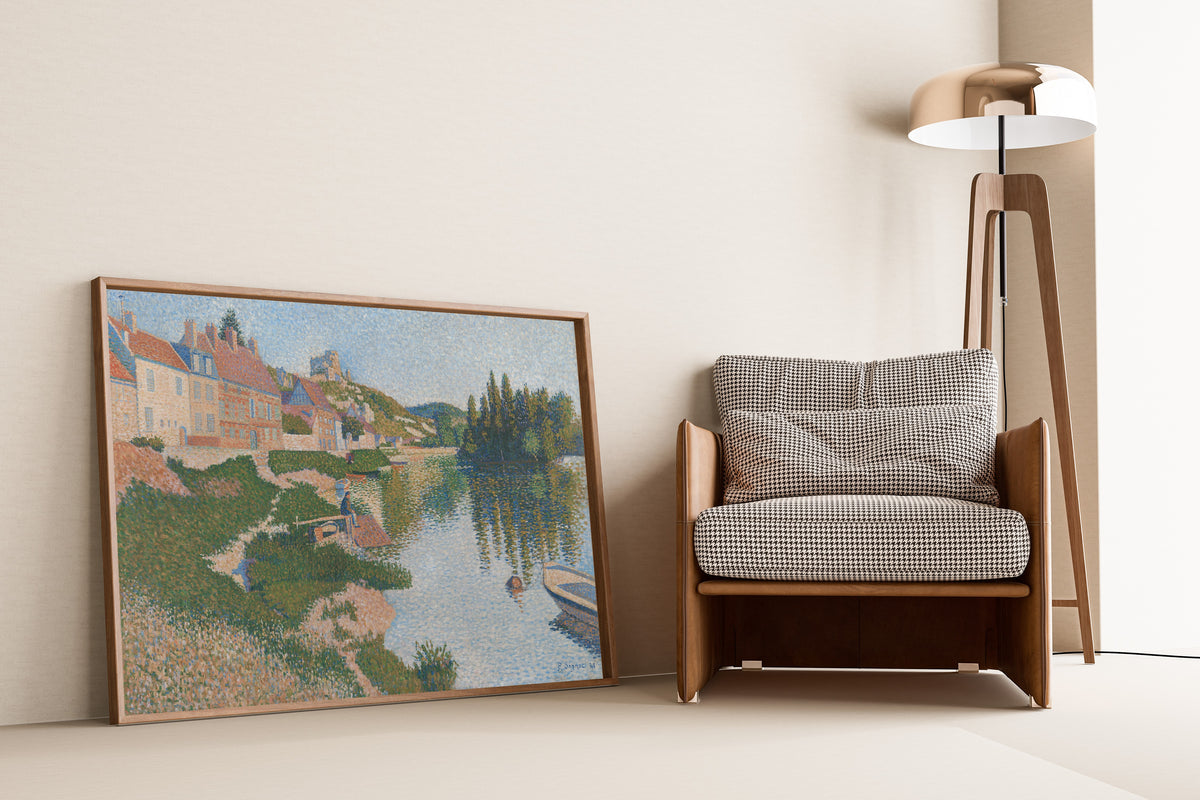 Framed art print of Les Andelys (1886) by Paul Signac, leaning against a wall beside an armchair and a floor lamp