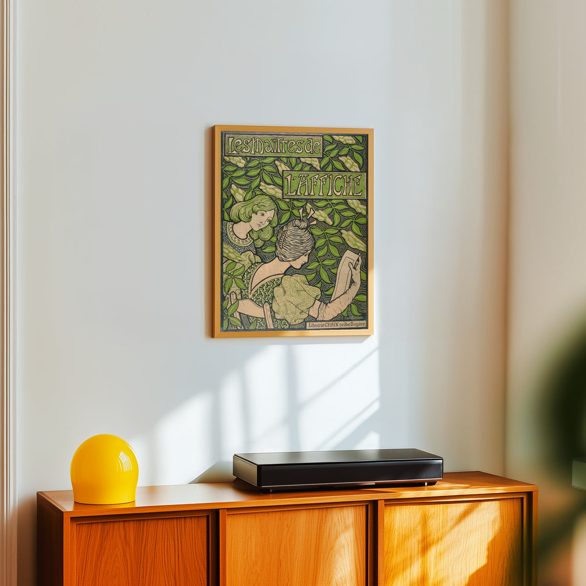 Framed art print of Les Maîtres de l'Affiche (cover) by Paul Berthon, in a light wood frame on a white wall above an orange sideboard