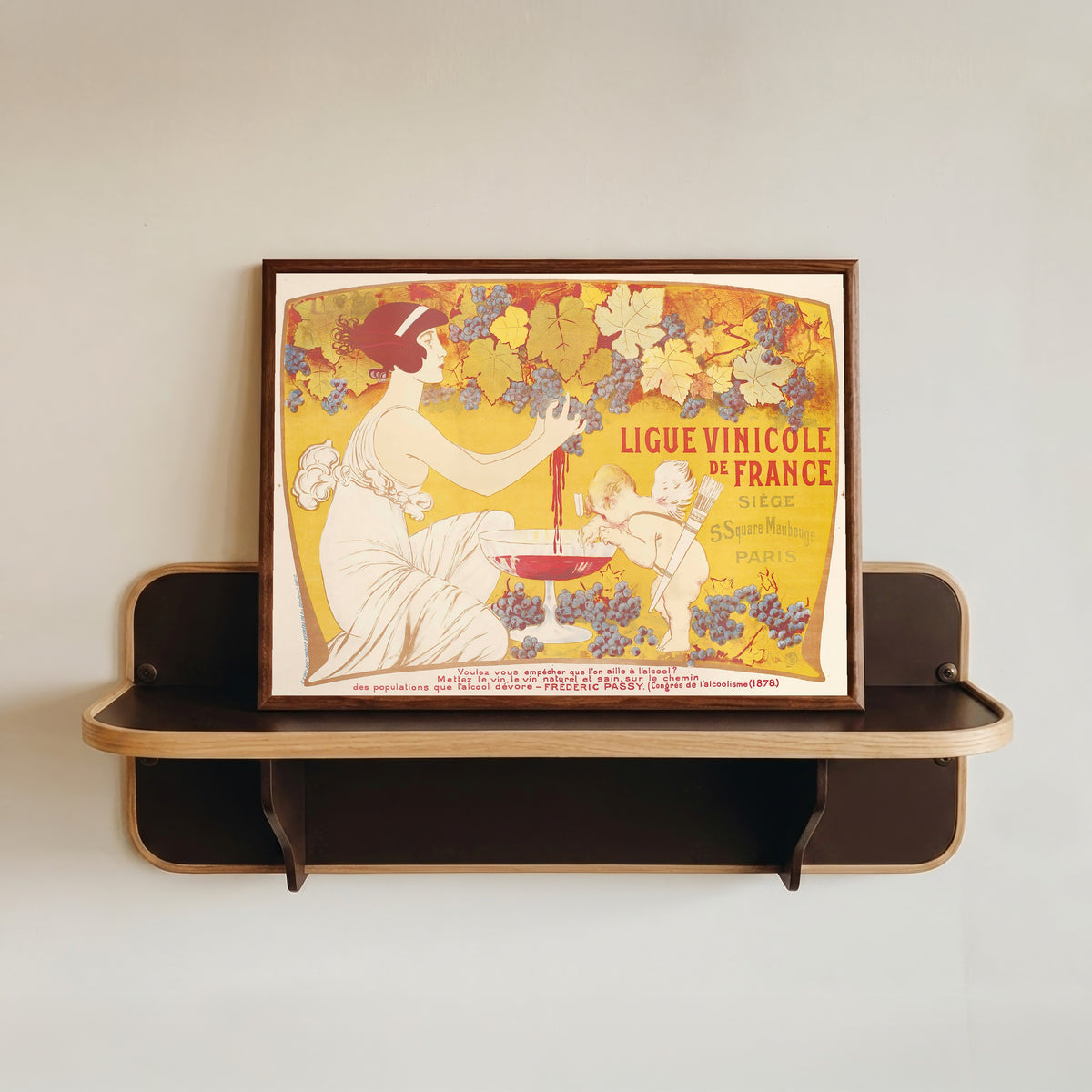 Framed art print of Ligue Vinicole de France by Manuel Orazi, in a dark wood frame resting on a wall shelf