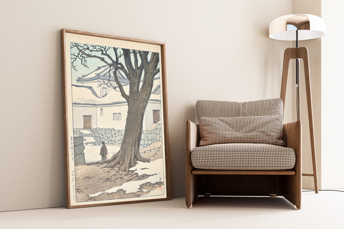 Framed art print of Lingering Snow at Hikone Castle by Kawase Hasui, leaning against a wall beside an armchair and a floor lamp