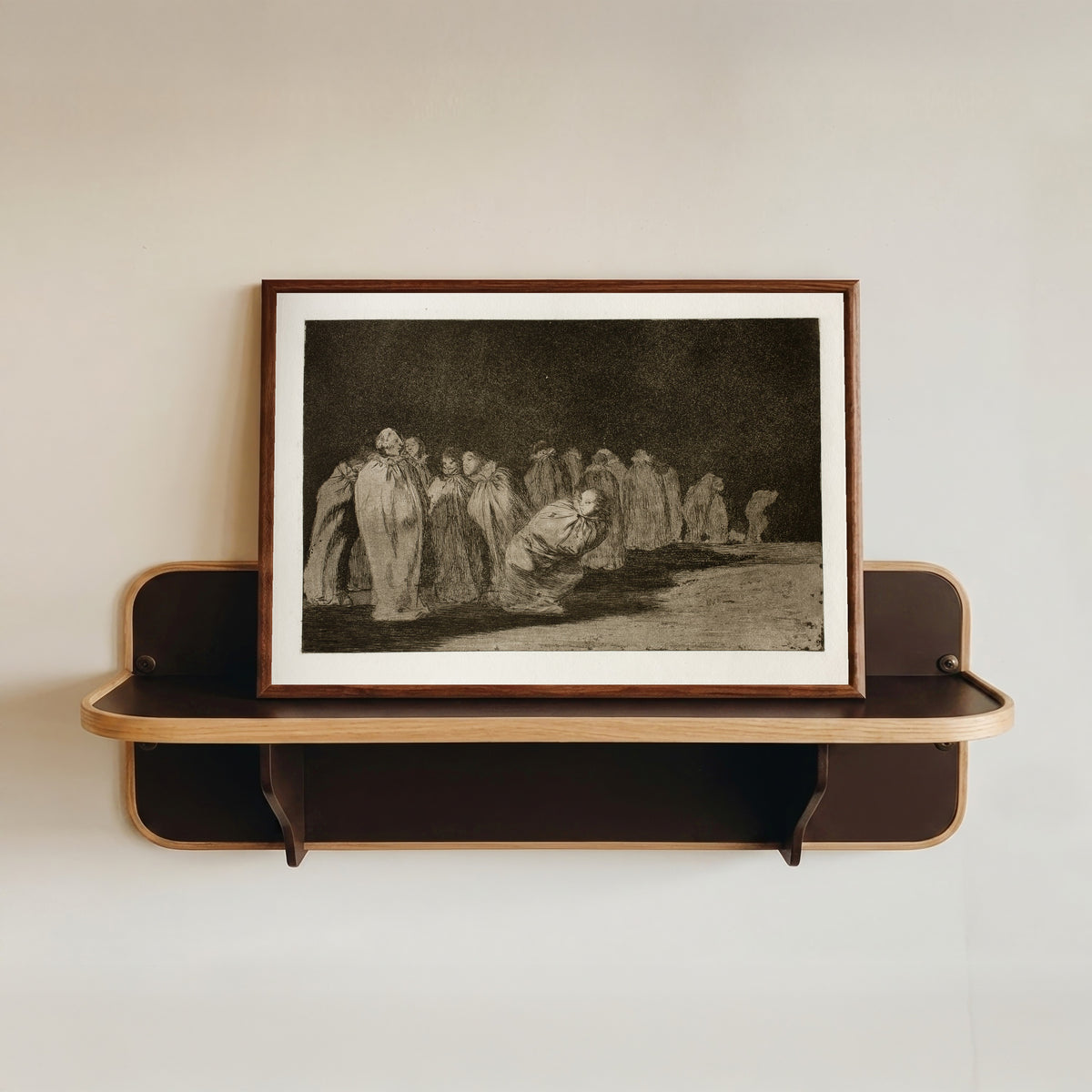 Framed art print of Los ensacados (The Men in Sacks), from Los Disparates by Francisco de Goya, in a dark wood frame resting on a wall shelf