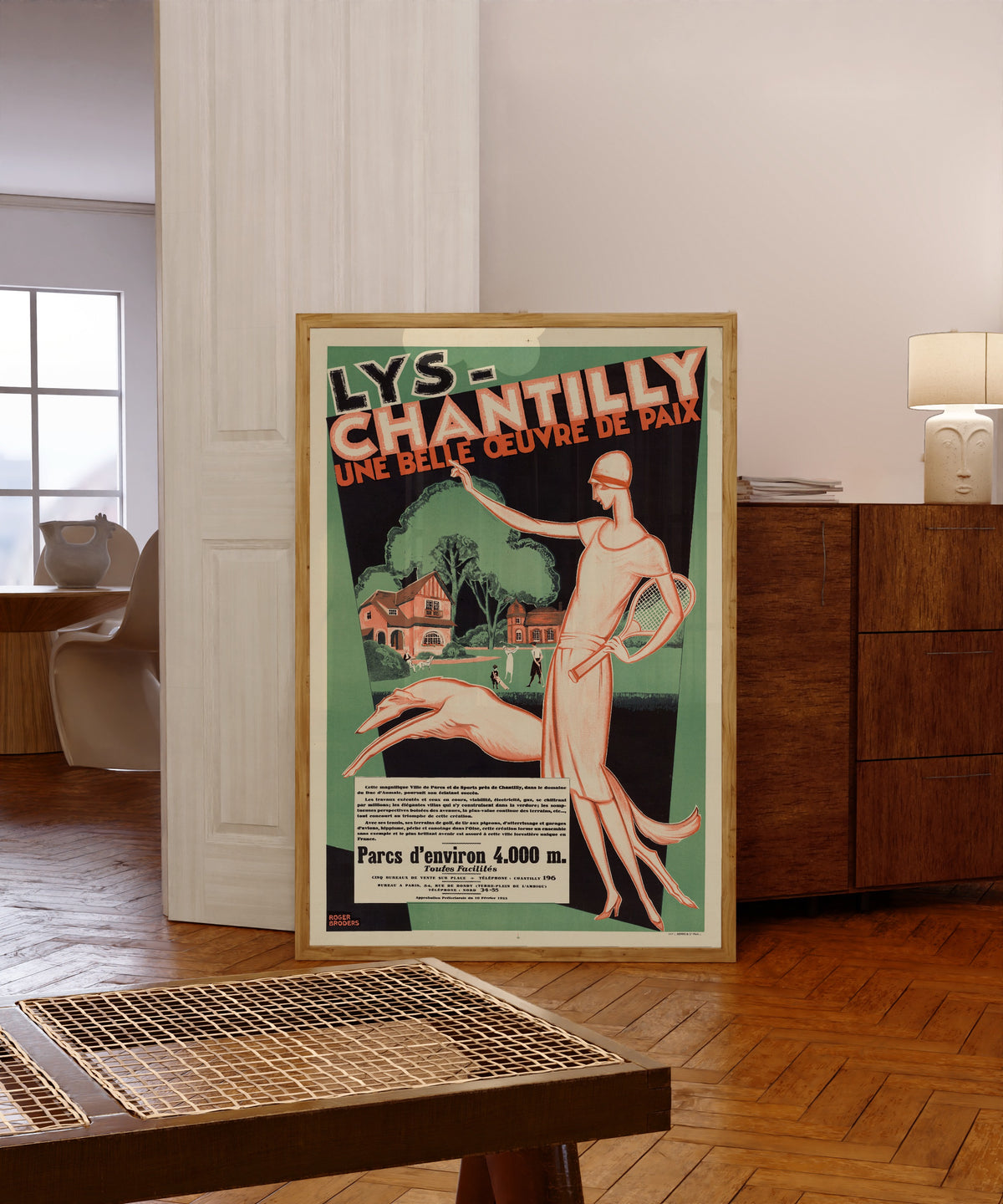 Framed art print of Lys-Chantilly: une belle œuvre de paix by Roger Broders, in a light wood frame leaning in a warm room with a parquet floor