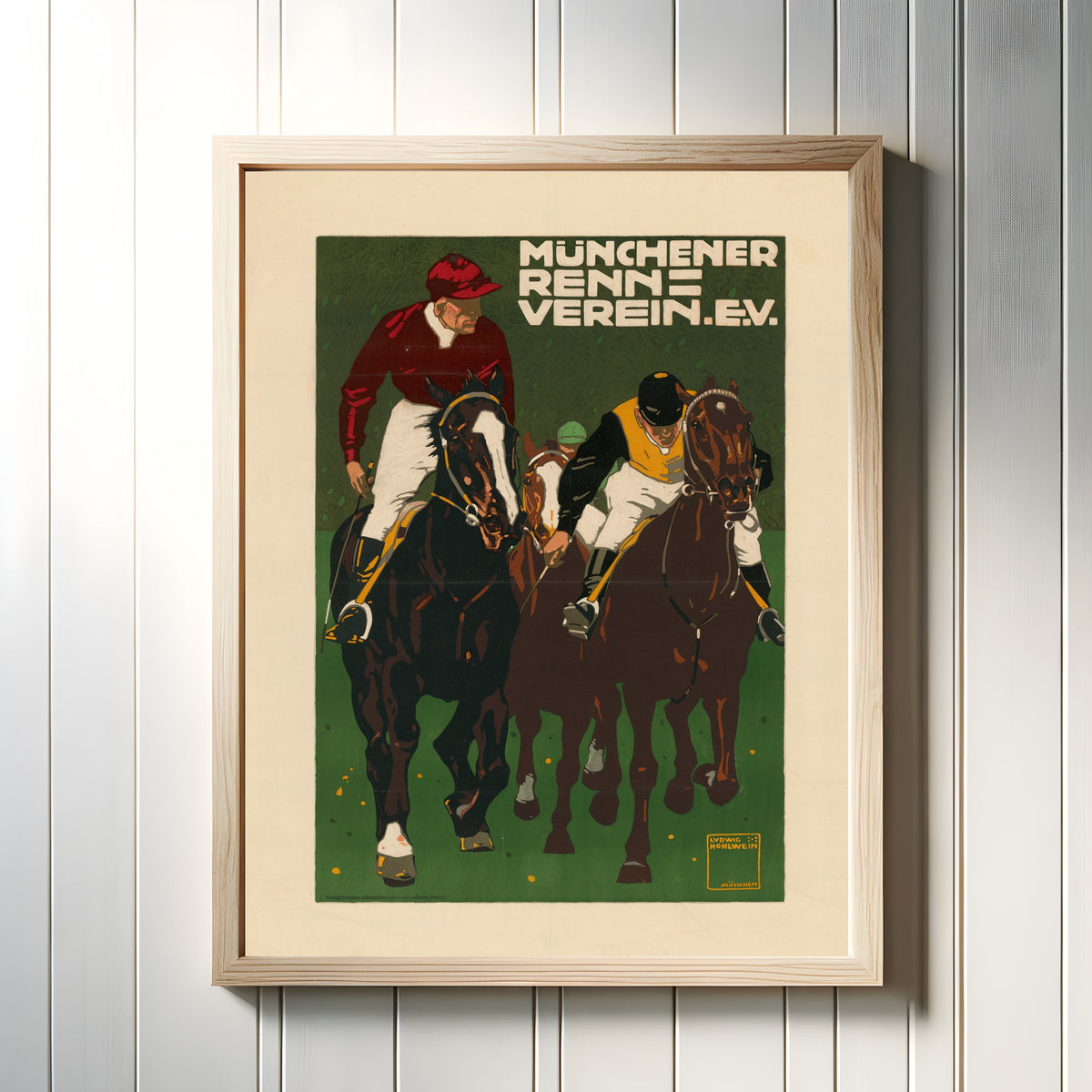 Framed art print of Münchener Rennverein e.V. by Ludwig Hohlwein, in a light wood frame on a white panelled wall