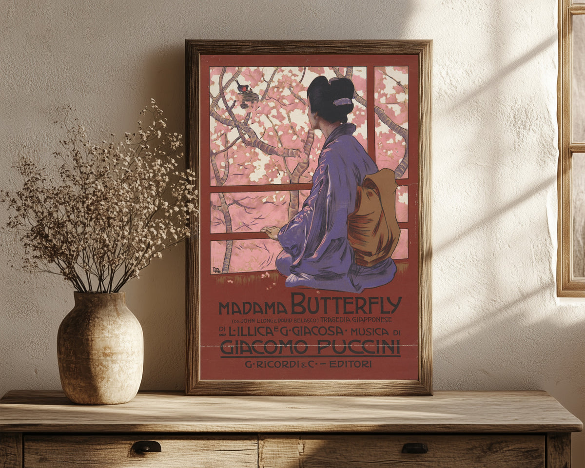 Framed art print of Madama Butterfly: Tragedia giapponese by Leopoldo Metlicovitz, in a dark wood frame leaning on a rustic console beside dried flowers