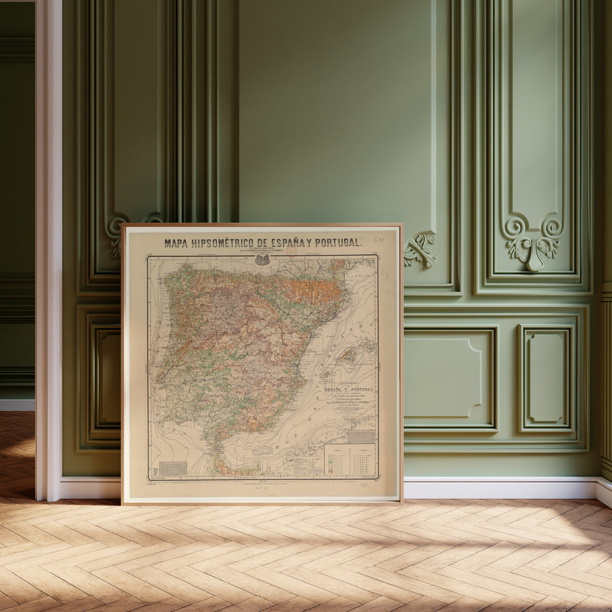 Mapa hipsométrico de España y Portugal by Federico de Botella y de Hornos — framed and leaning against olive-green panelling on a herringbone floor