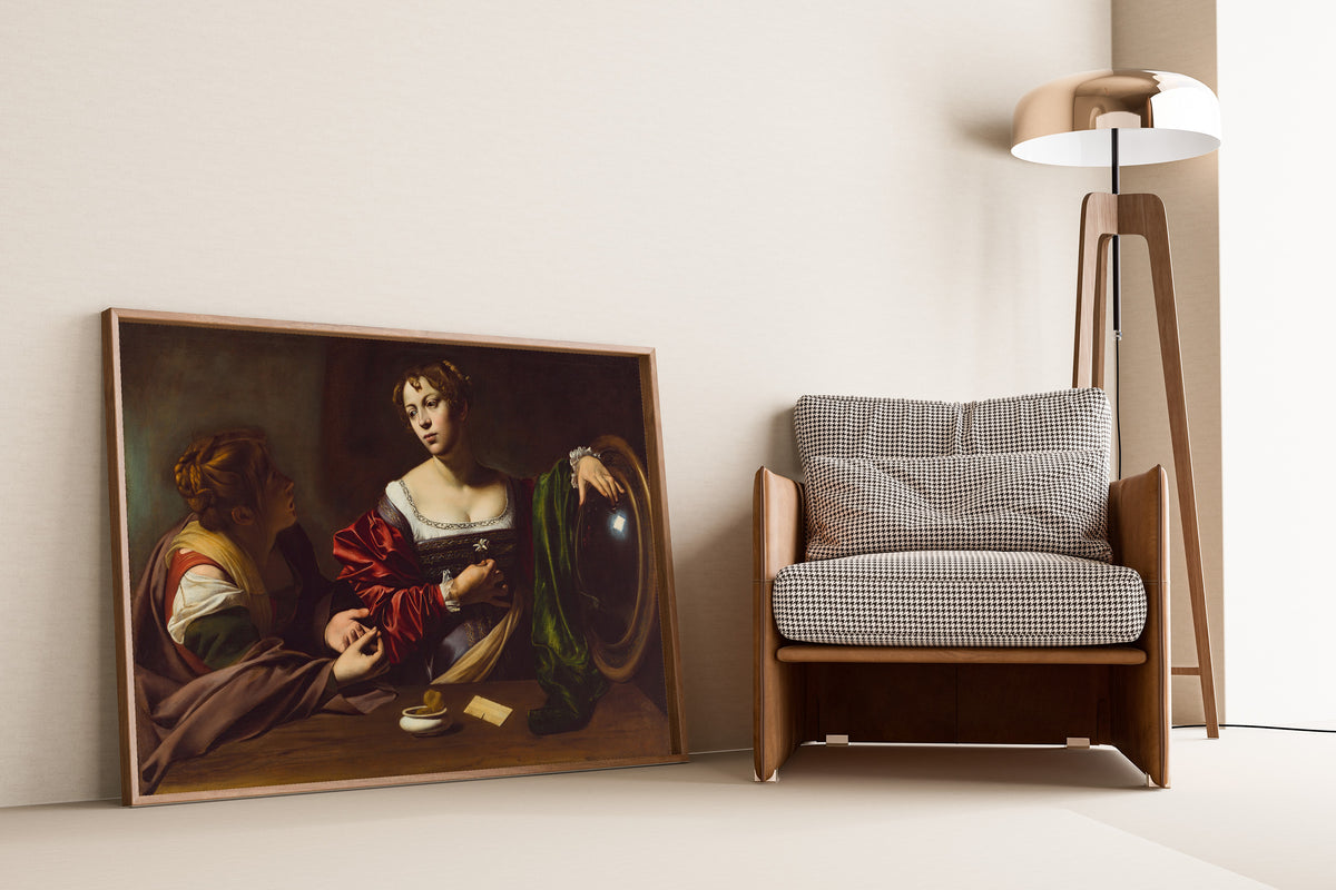Framed art print of Martha and Mary Magdalene by Caravaggio, leaning against a wall beside an armchair and a floor lamp