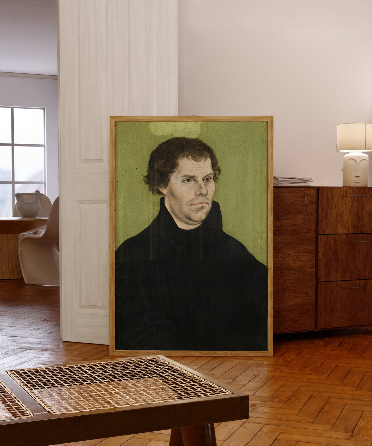 Framed art print of Martin Luther by Lucas Cranach the Elder, in a light wood frame leaning in a warm room with a parquet floor