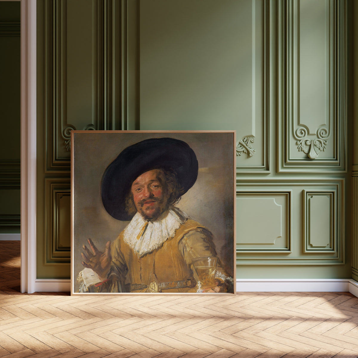Framed art print of Merry Drinker by Frans Hals, leaning against olive-green panelling on a herringbone floor