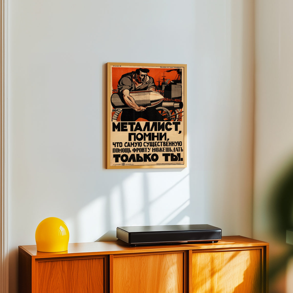 Framed art print of Metalworker, remember that only you can give the… by Vasily Kostyanitsyn, in a light wood frame on a white wall above an orange sideboard