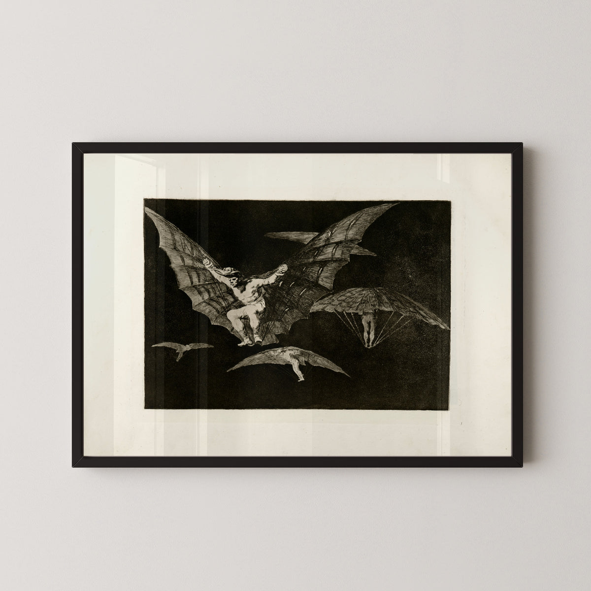 Framed art print of Modo de volar (A Way of Flying), from Los Disparates by Francisco de Goya, in a black frame on a pale wall