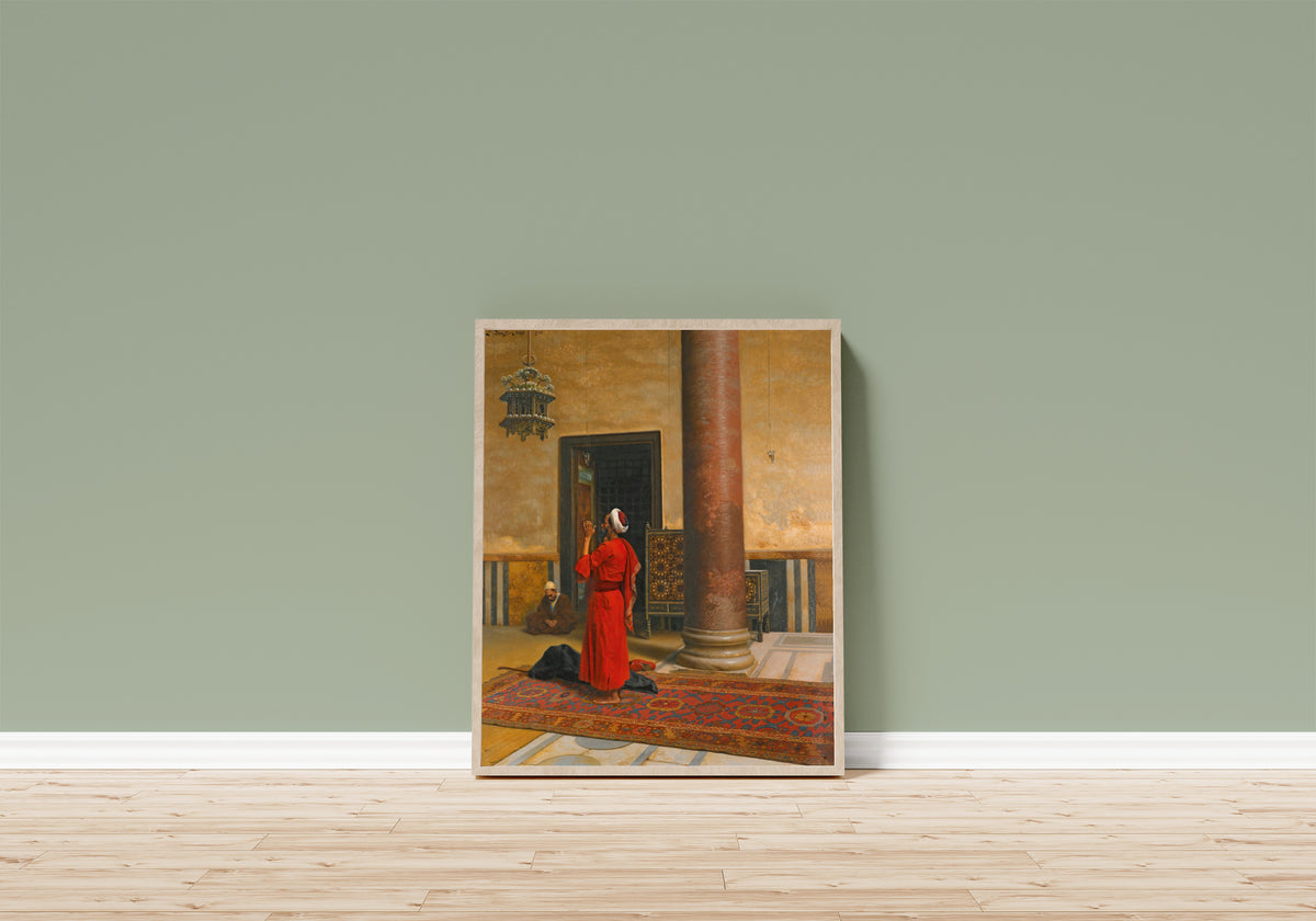 Framed art print of Morning Prayers by Ludwig Deutsch, in a light wood frame leaning on a sage green wall above a wooden floor