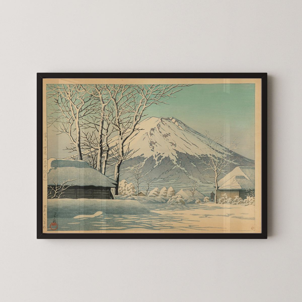 Framed art print of Mount Fuji, Clearing after a Snowfall, Oshino by Kawase Hasui, in a black frame on a pale wall