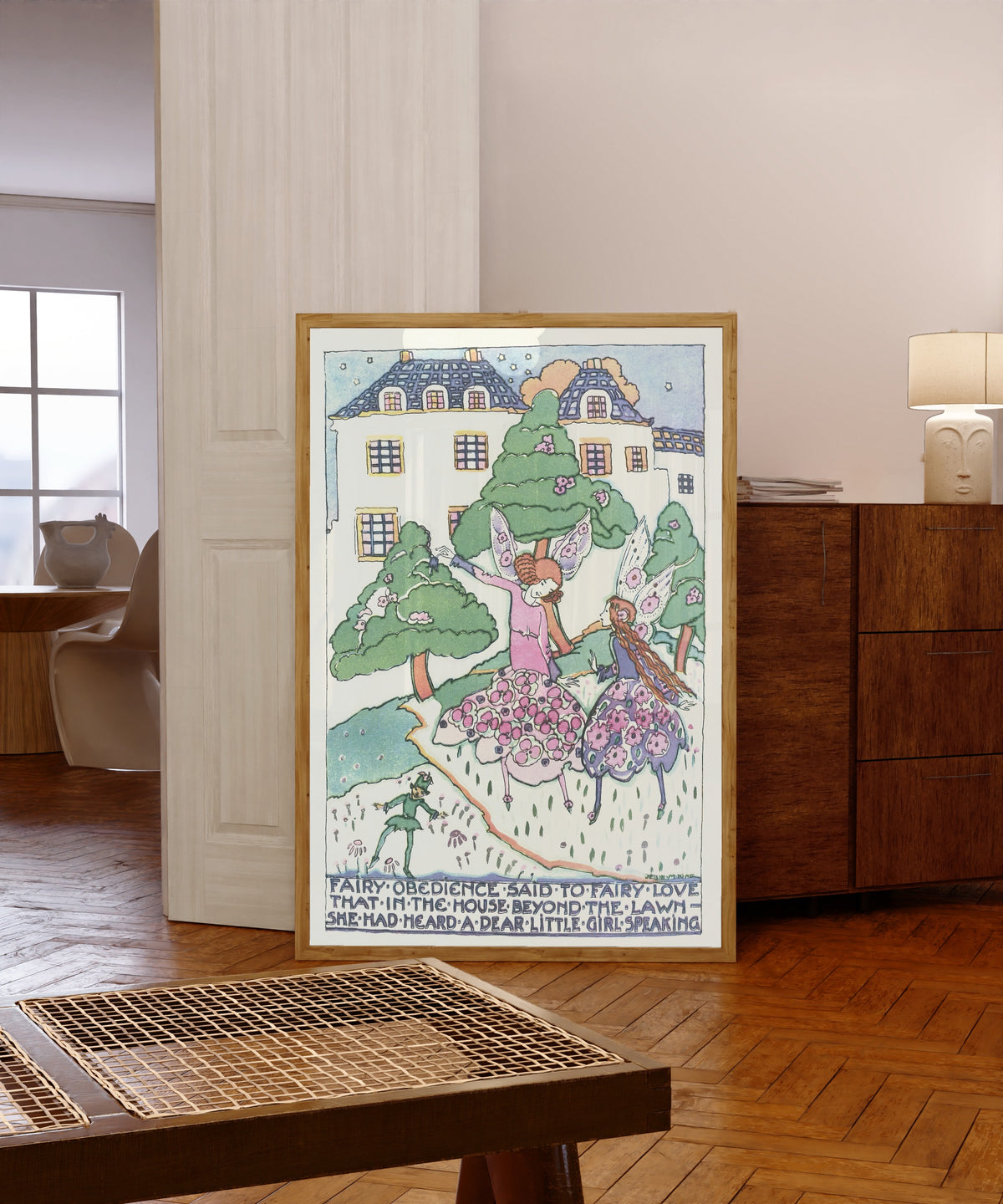 Framed art print of Mummy's Bedtime Story Book: Fairy Obedience Said to… by Jessie M. King, in a light wood frame leaning in a warm room with a parquet floor