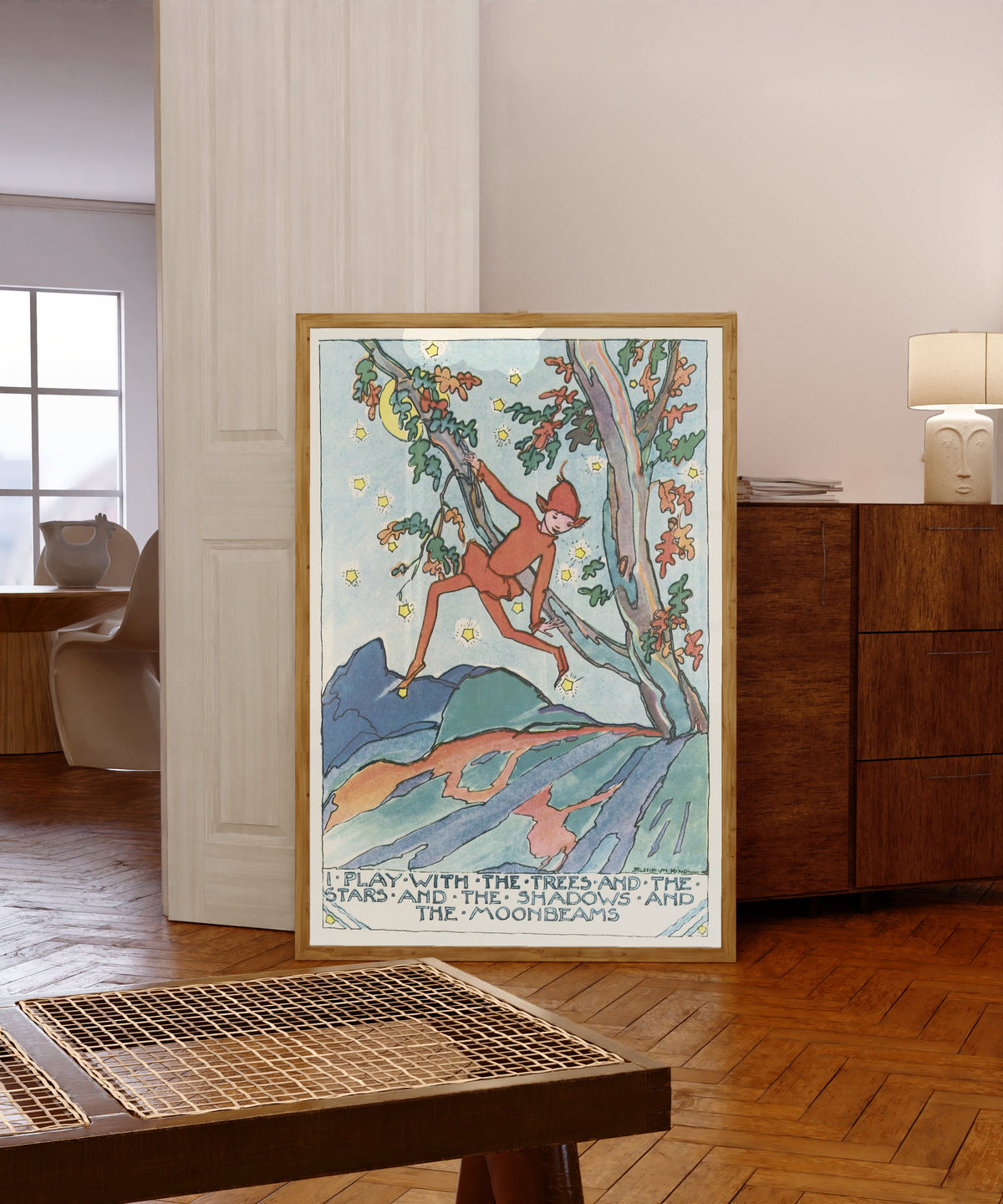 Framed art print of Mummy's Bedtime Story Book: I Play with the Trees and… by Jessie M. King, in a light wood frame leaning in a warm room with a parquet floor
