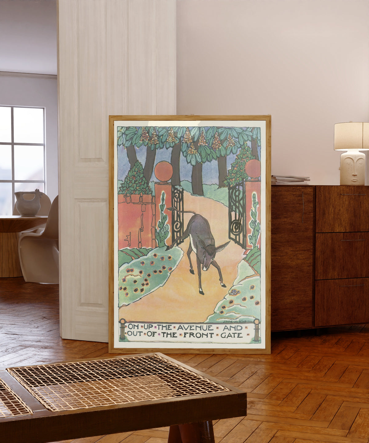 Framed art print of Mummy's Bedtime Story Book: On Up the Avenue and Out… by Jessie M. King, in a light wood frame leaning in a warm room with a parquet floor